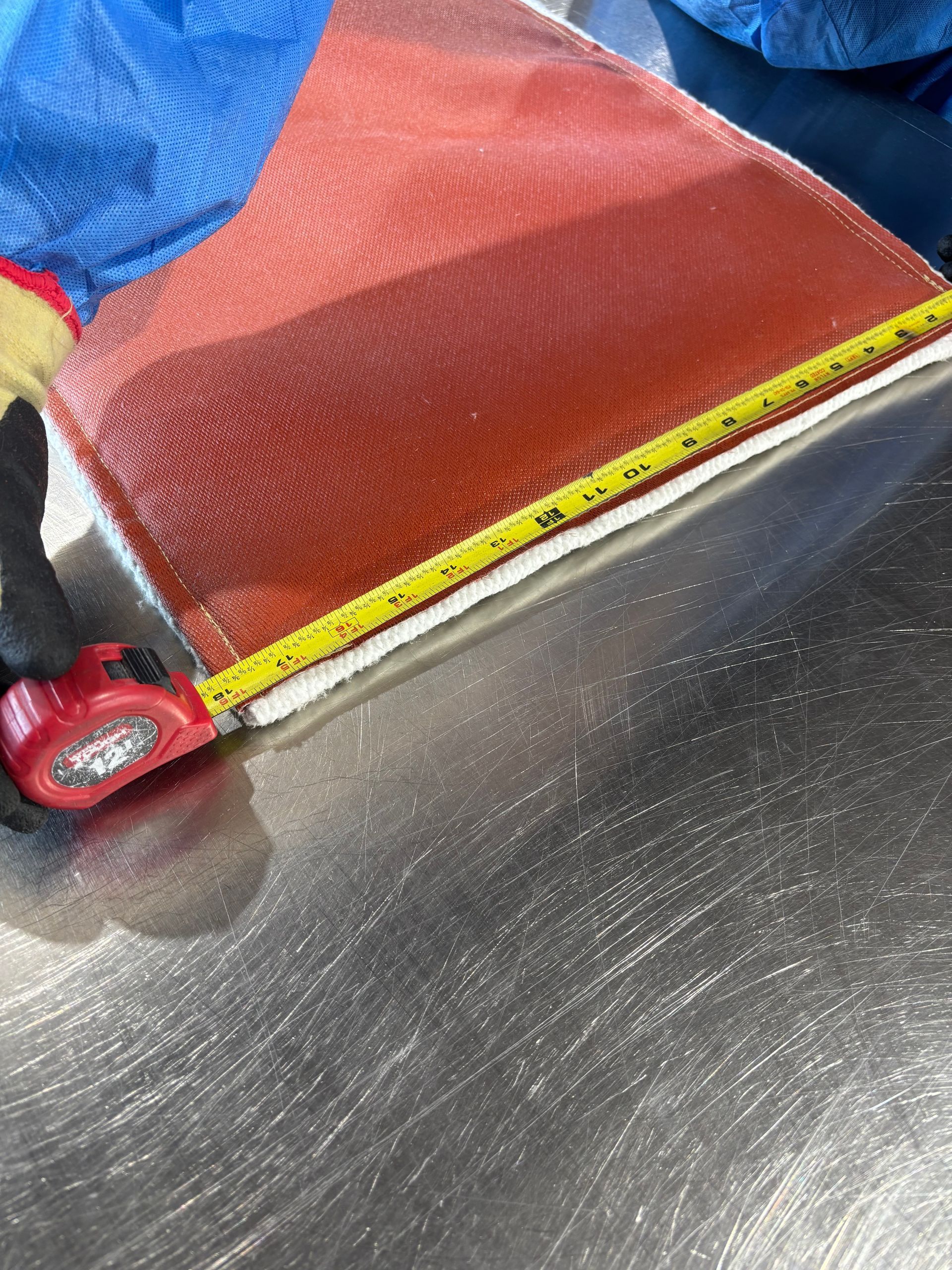 Close-up of a red fabric bag being measured with a yellow tape measure on a metallic surface.