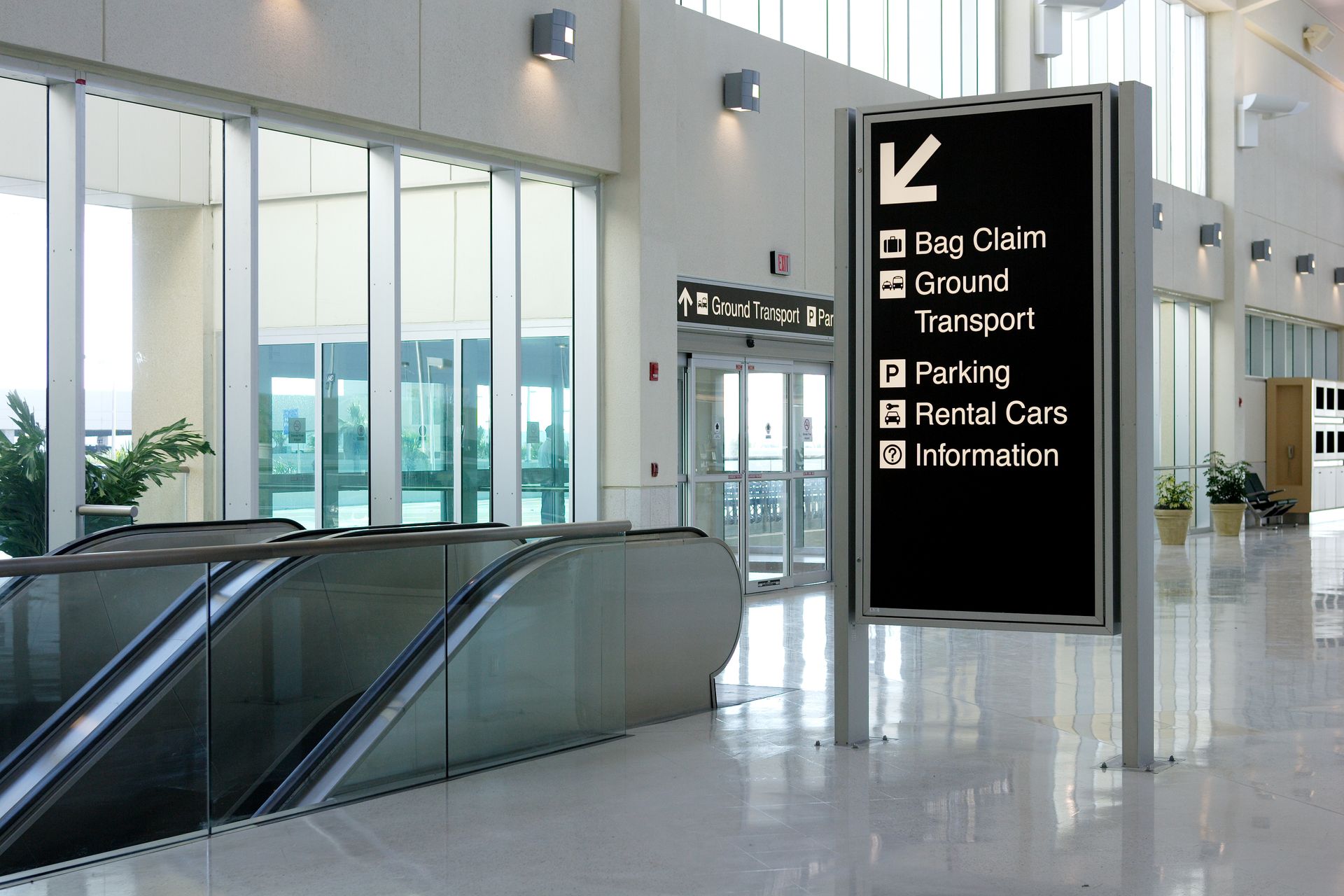 Airport terminal with directional sign: Bag Claim, Ground Transport, Parking, Rental Cars, and Information.
