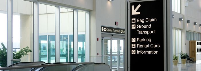 Airport interior with directional sign for bag claim, ground transport, parking, rental cars, and information.
