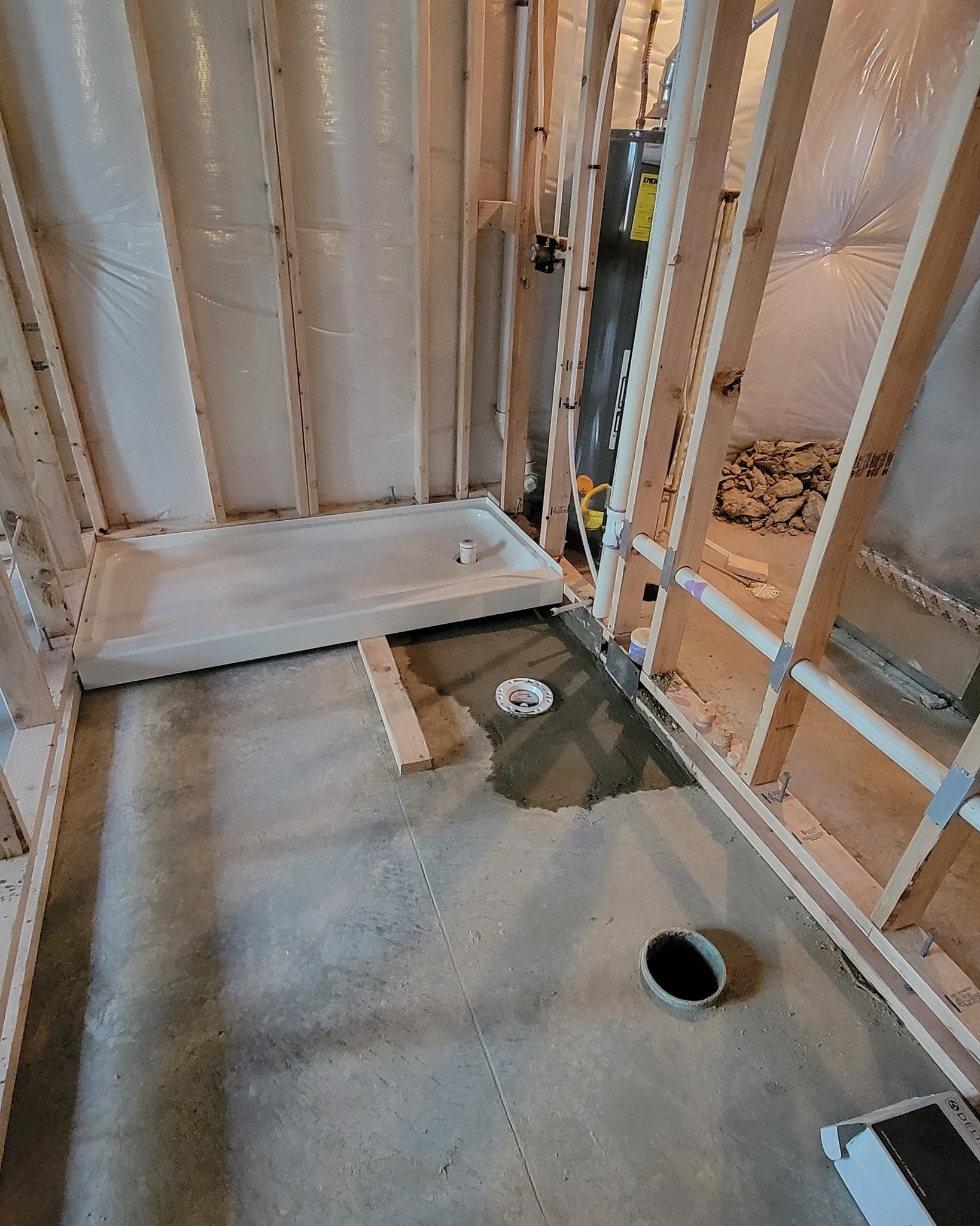 Bathroom under construction, with shower base installed, framing, and concrete floor.