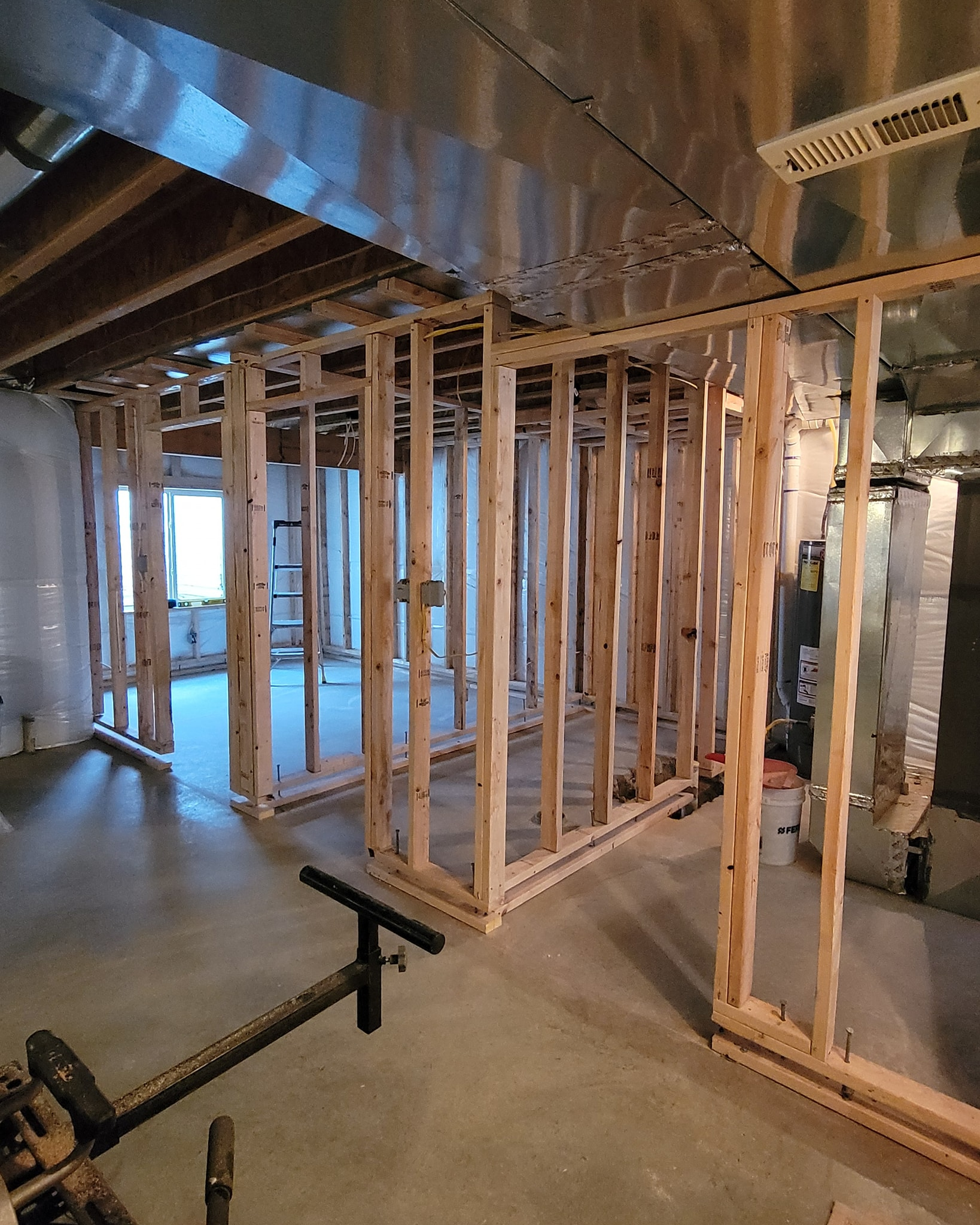 Unfinished basement with wooden framing for walls and ceiling, on a concrete floor.