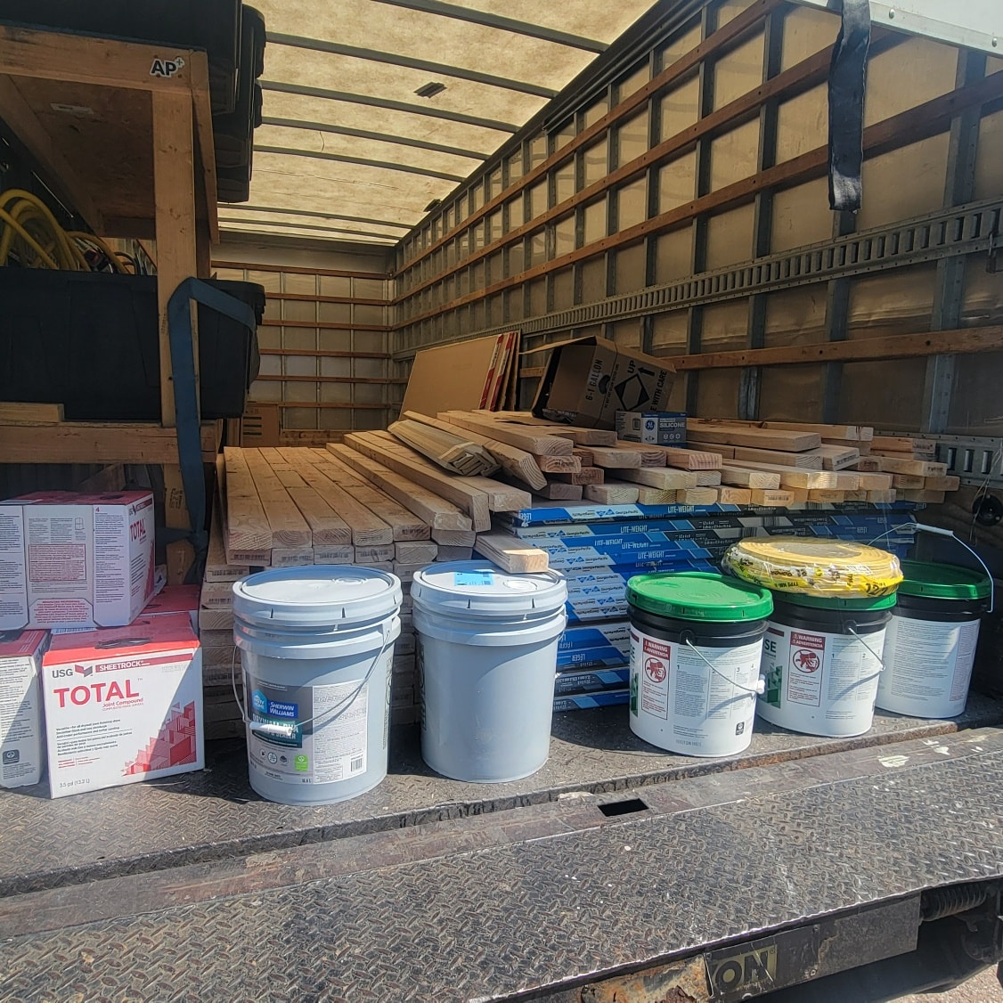 Interior of a truck bed loaded with paint buckets, lumber, and boxes of supplies.