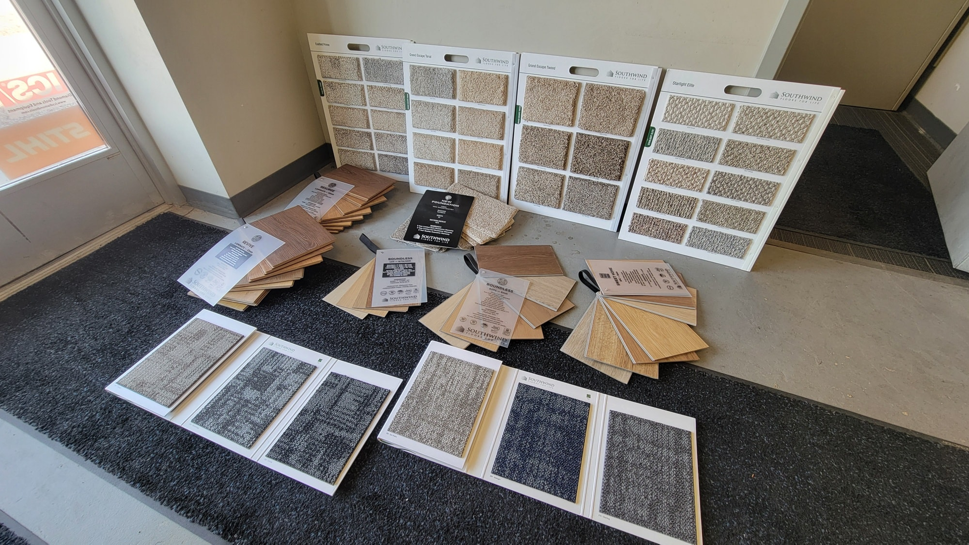 Carpet samples arranged on a dark rug inside a building, with white display boards and brochures.