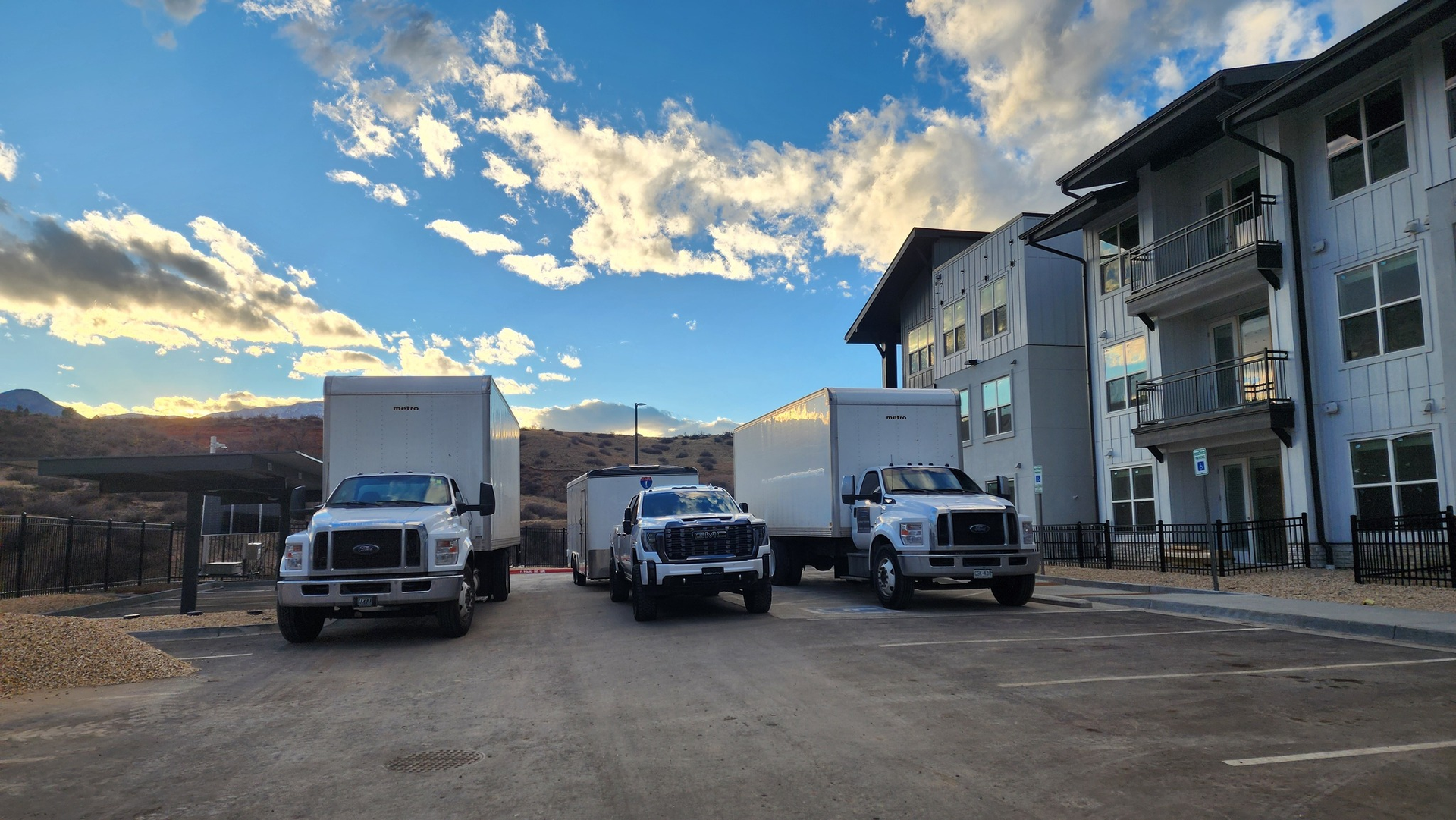 Three moving trucks parked in front of an apartment building on a sunny day.