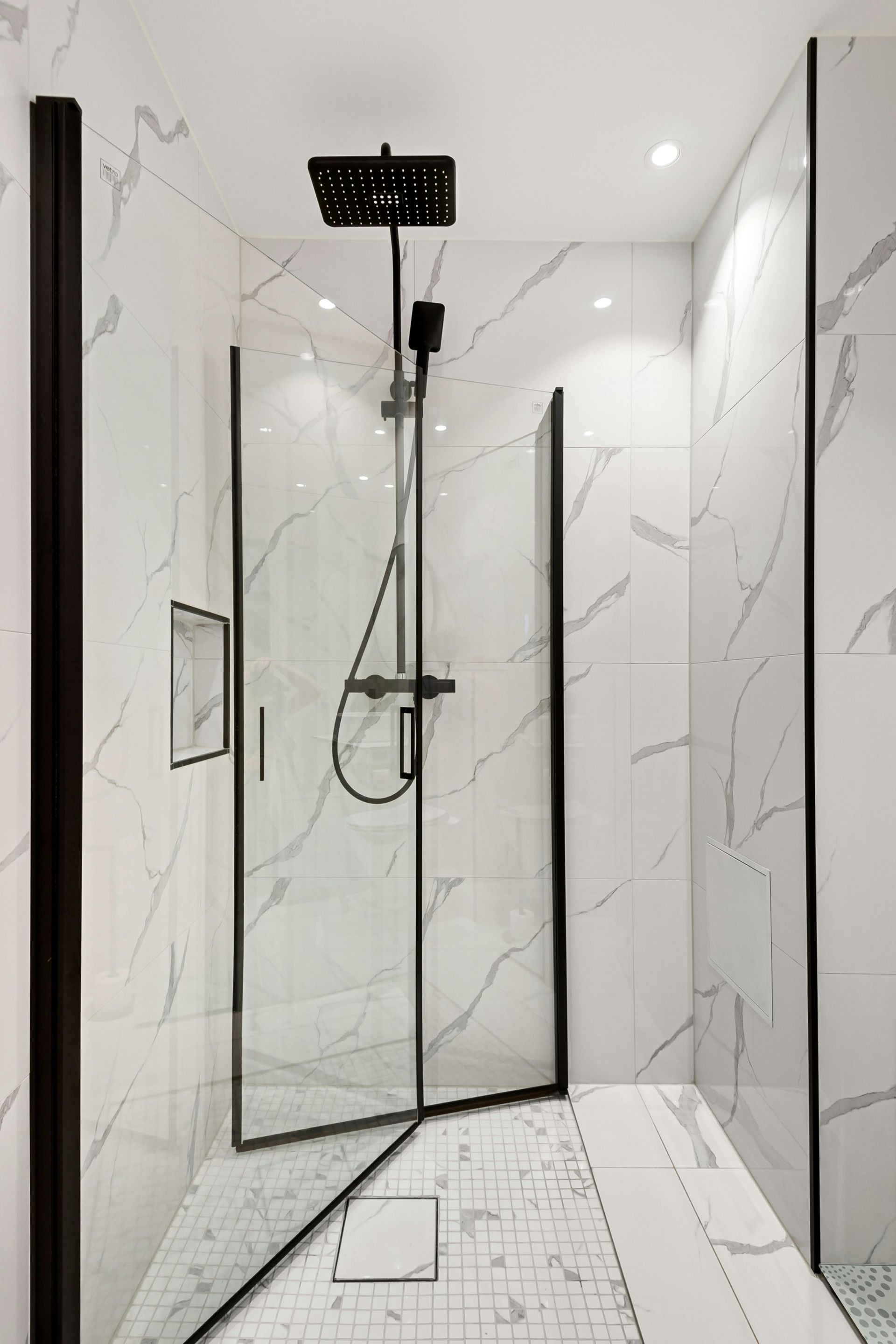 Modern shower with black fixtures and marble-look white tile.
