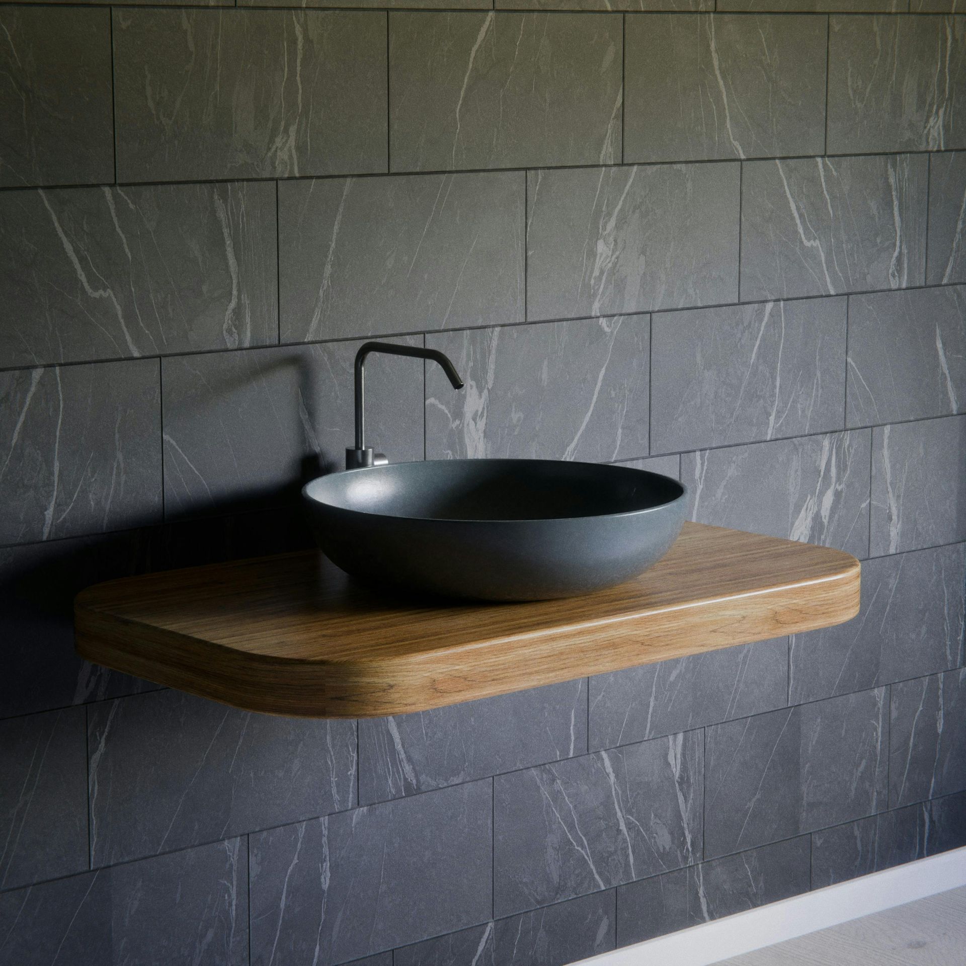 Dark gray vessel sink on a floating wooden shelf against gray tile wall. Black faucet.