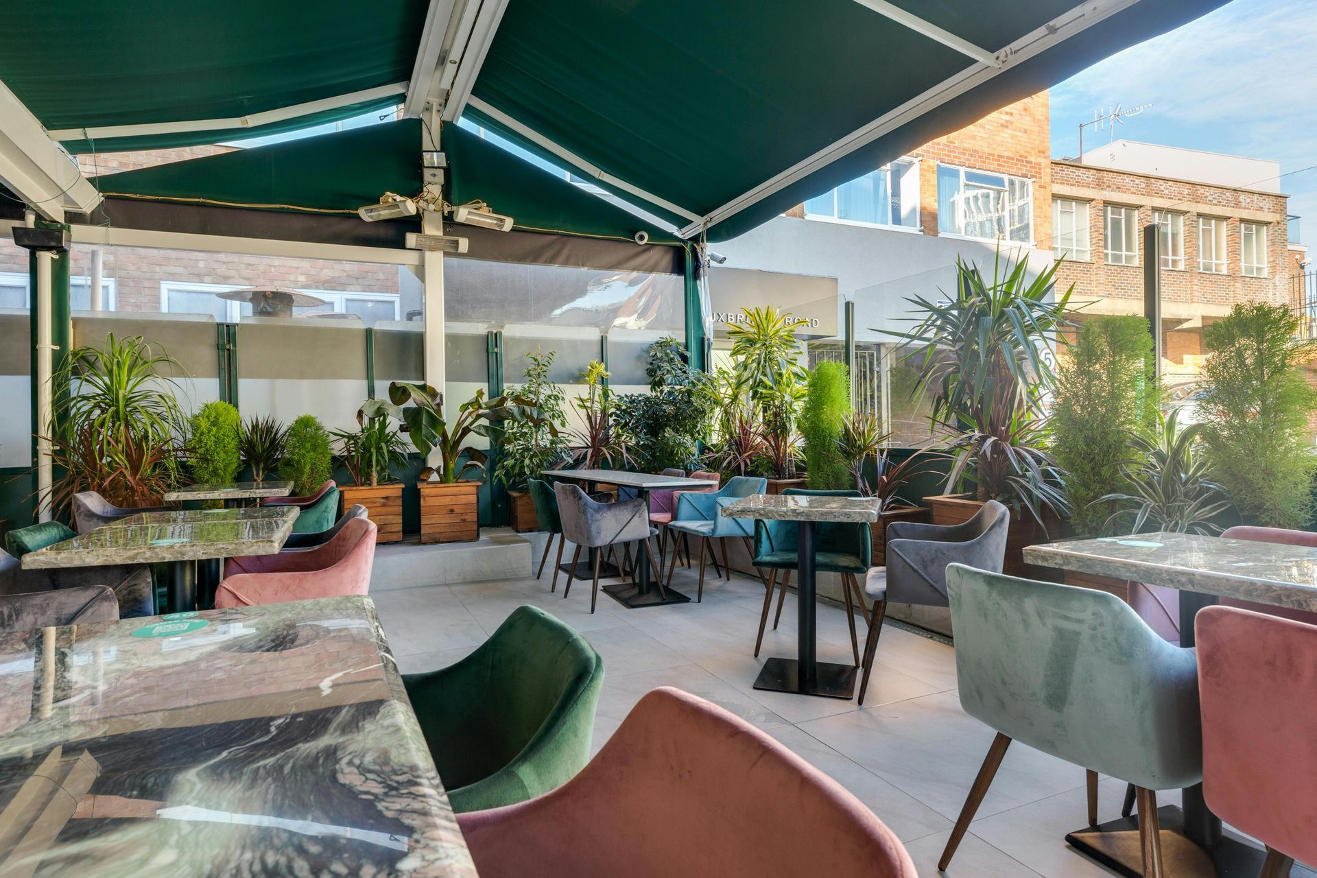 Rooftop restaurant patio with tables, chairs, plants, and a green awning.