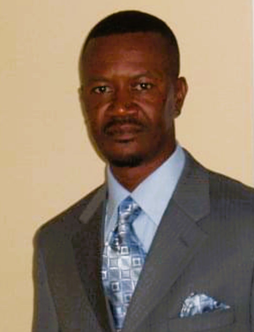 Man in a gray suit, light blue shirt, patterned tie, and pocket square. Neutral expression.