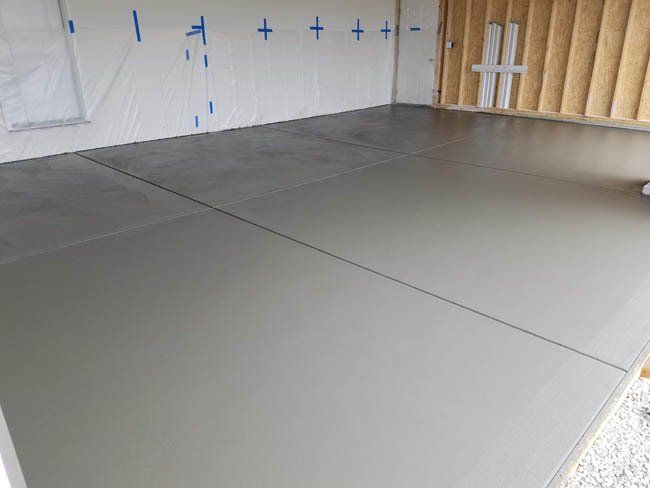 A gray concrete floor in a garage with a white wall.