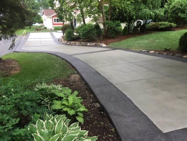 A concrete driveway leading to a house surrounded by plants