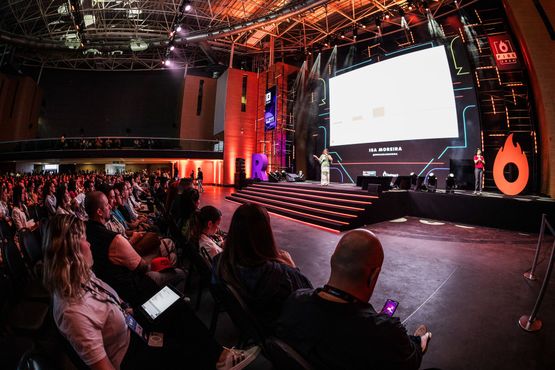 Um grande grupo de pessoas está sentado em frente a um palco em uma conferência.