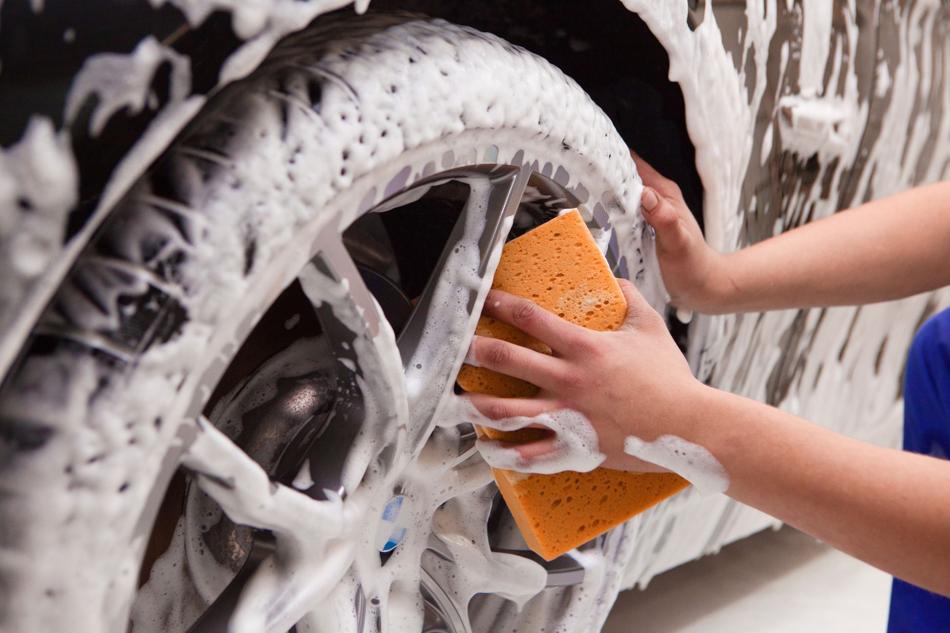 A person is washing a car wheel with a sponge.