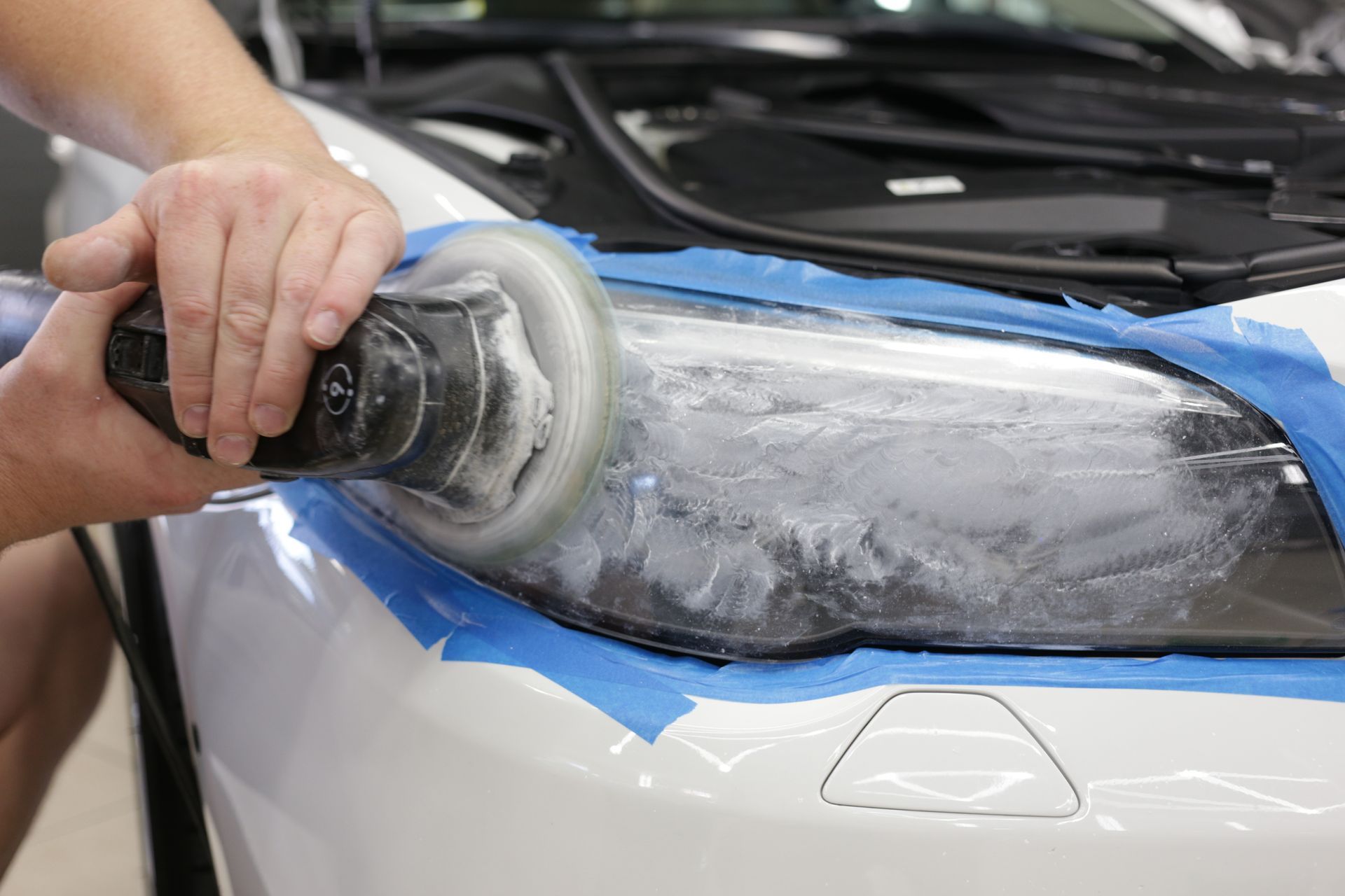 A person is polishing a car headlight with a polisher.