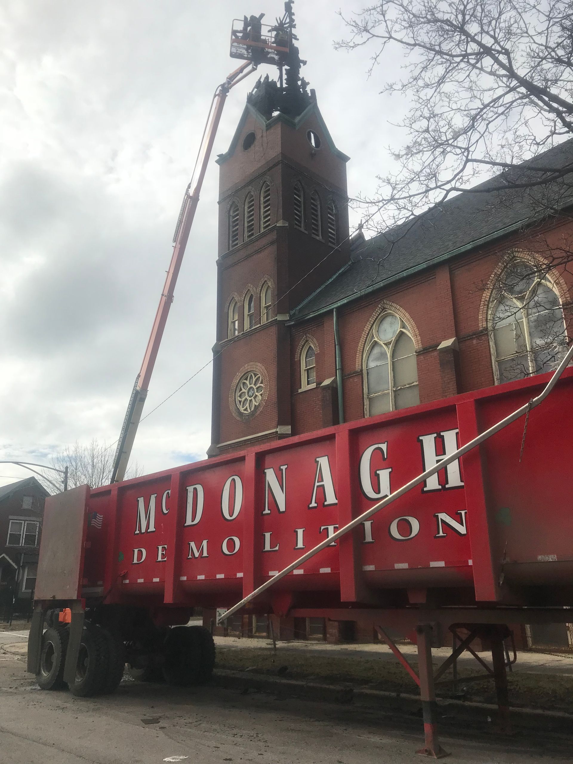 A red demolition truck is parked in front of a church