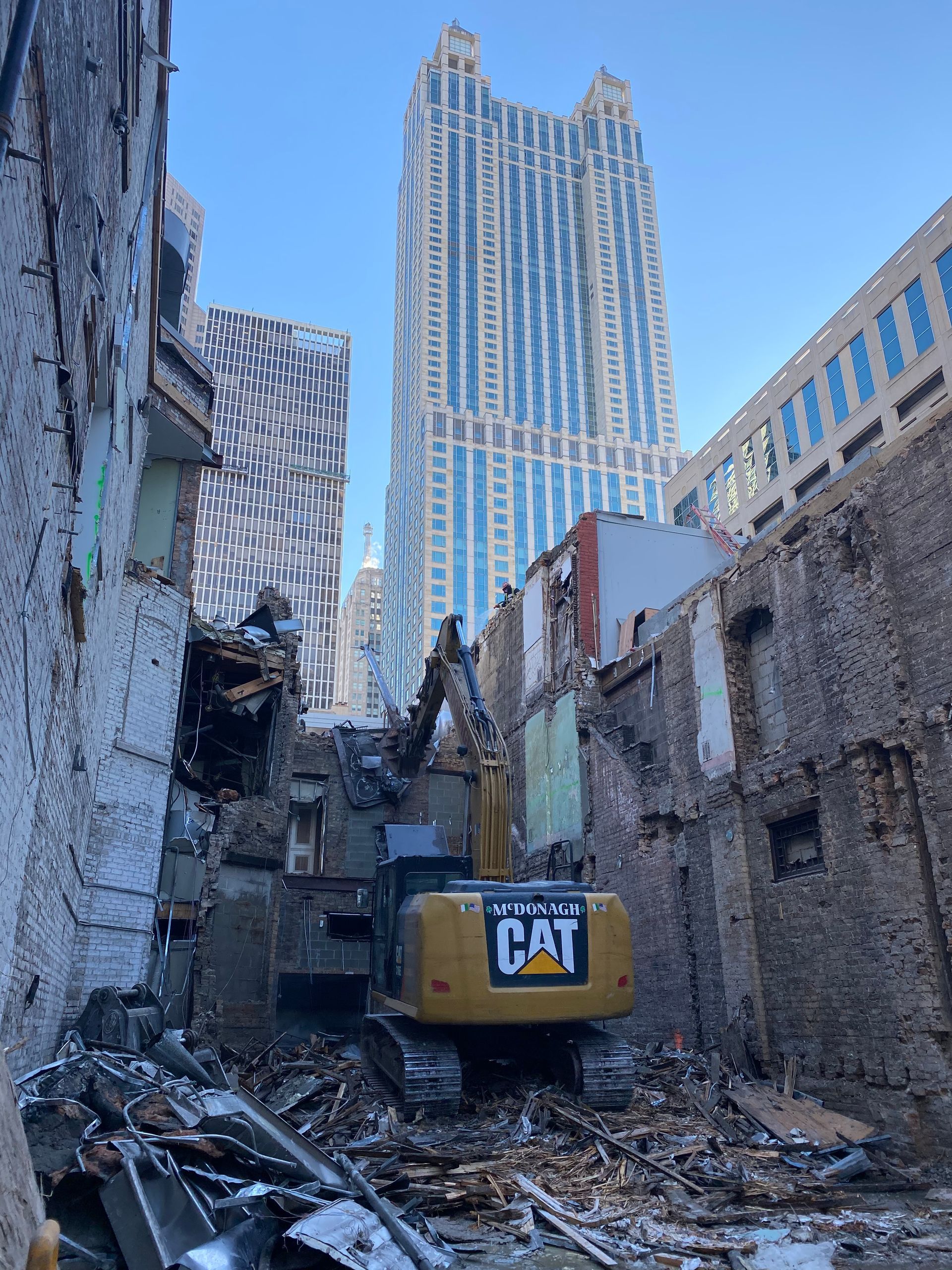 A cat excavator is destroying a building in a city.