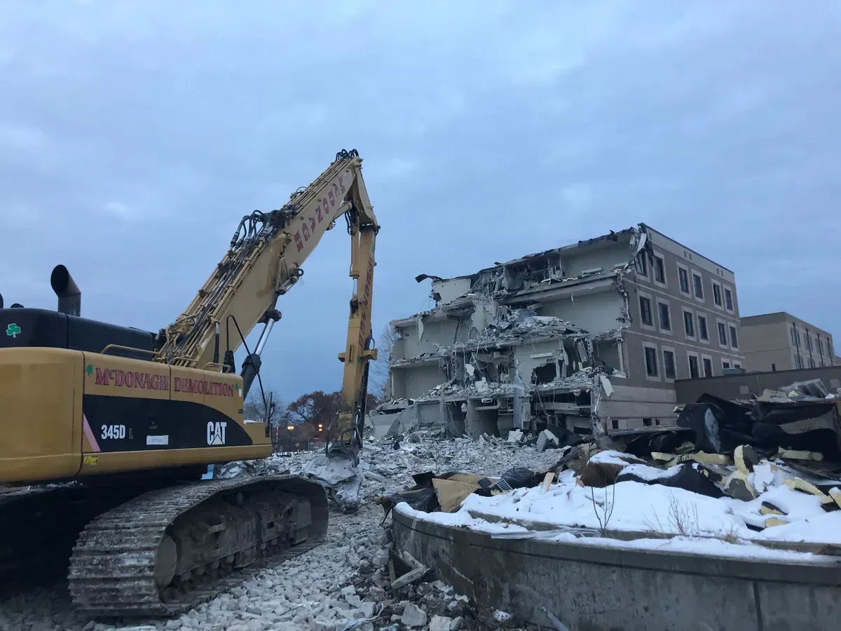 A large yellow excavator is demolishing a building in the snow.