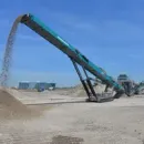 A conveyor belt is pouring sand into a pile of dirt.