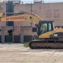 A yellow excavator is parked in front of a brick building.