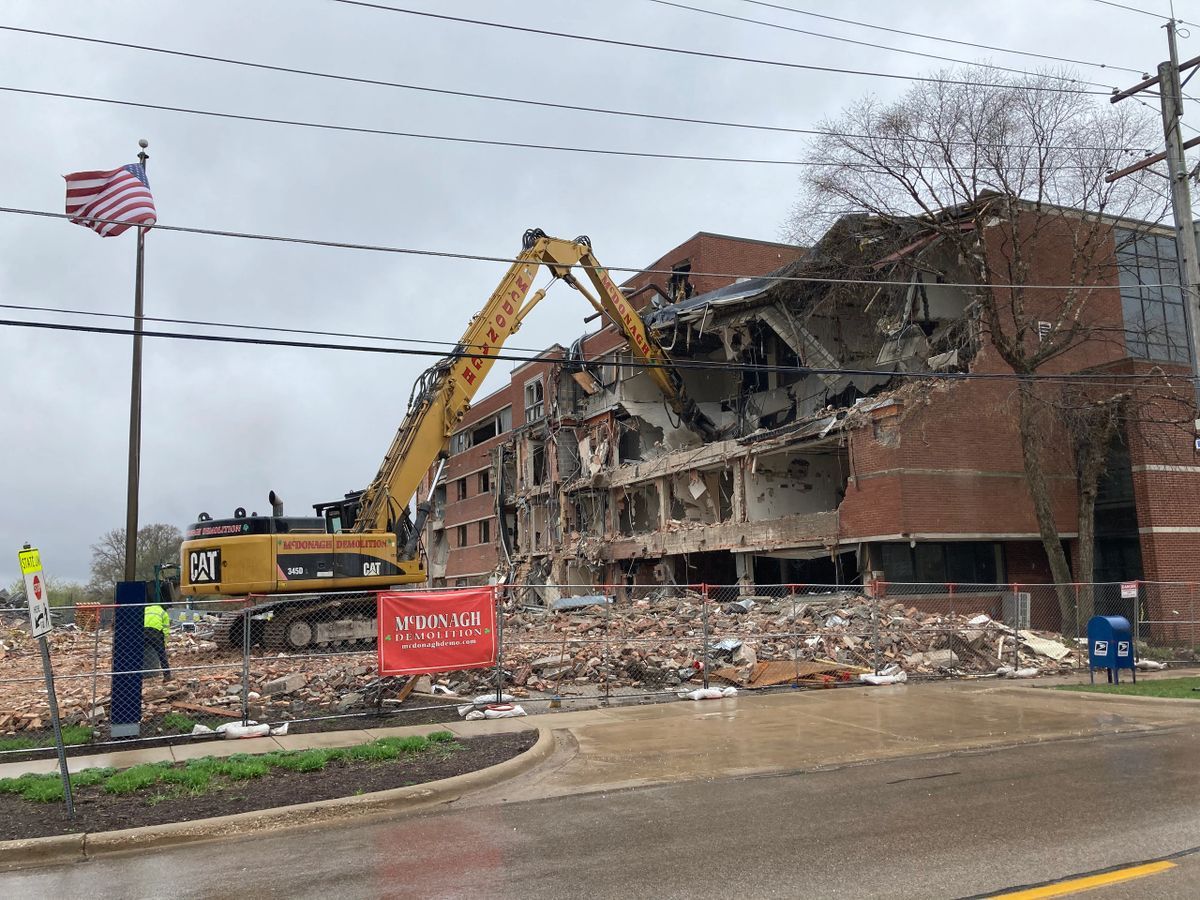 A large brick building is being demolished by a bulldozer.