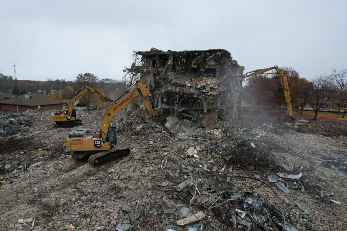 A large building is being demolished by a couple of bulldozers.