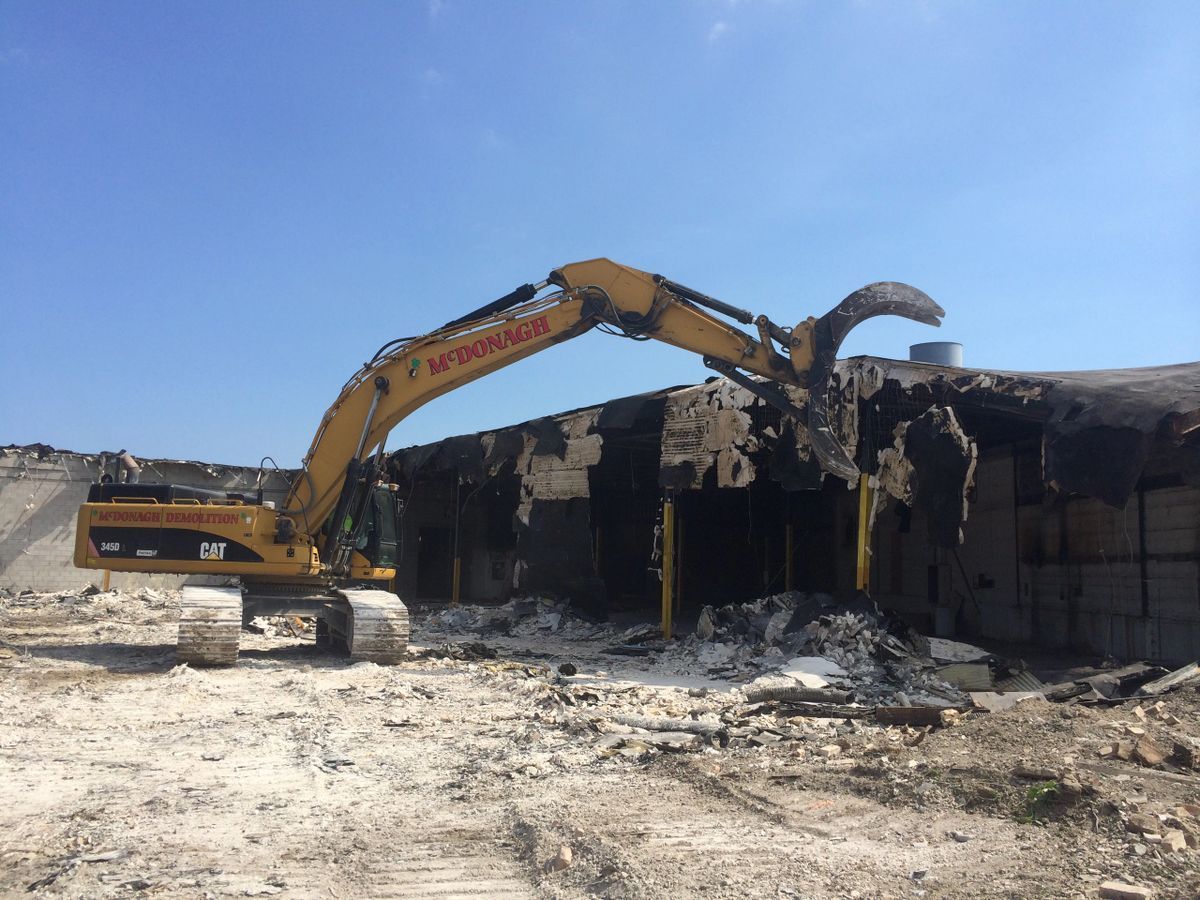 A large yellow excavator is demolishing a building.