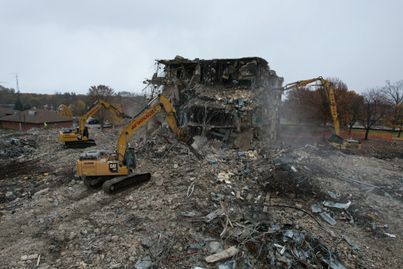 Two bulldozers are demolishing a building in a field.