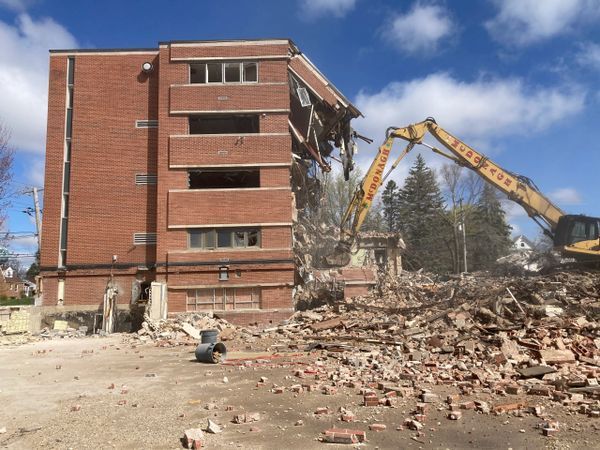 A large brick building is being demolished by a yellow excavator that says ' jcl ' on it