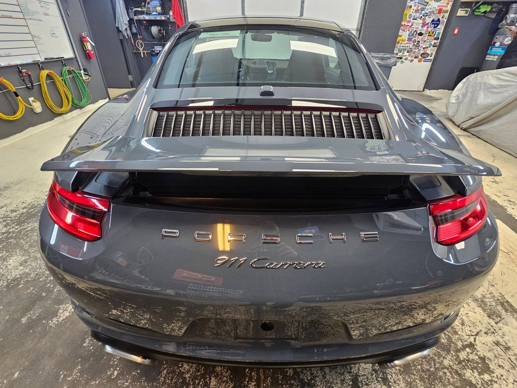 A gray porsche 911 carrera is parked in a garage.