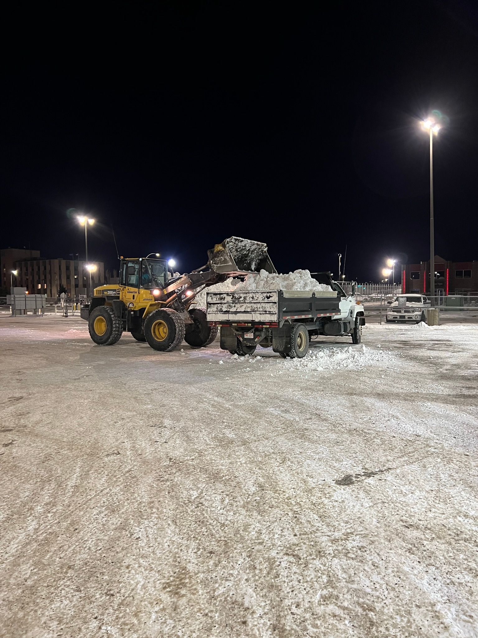 A couple of tractors are parked in a snowy parking lot at night.