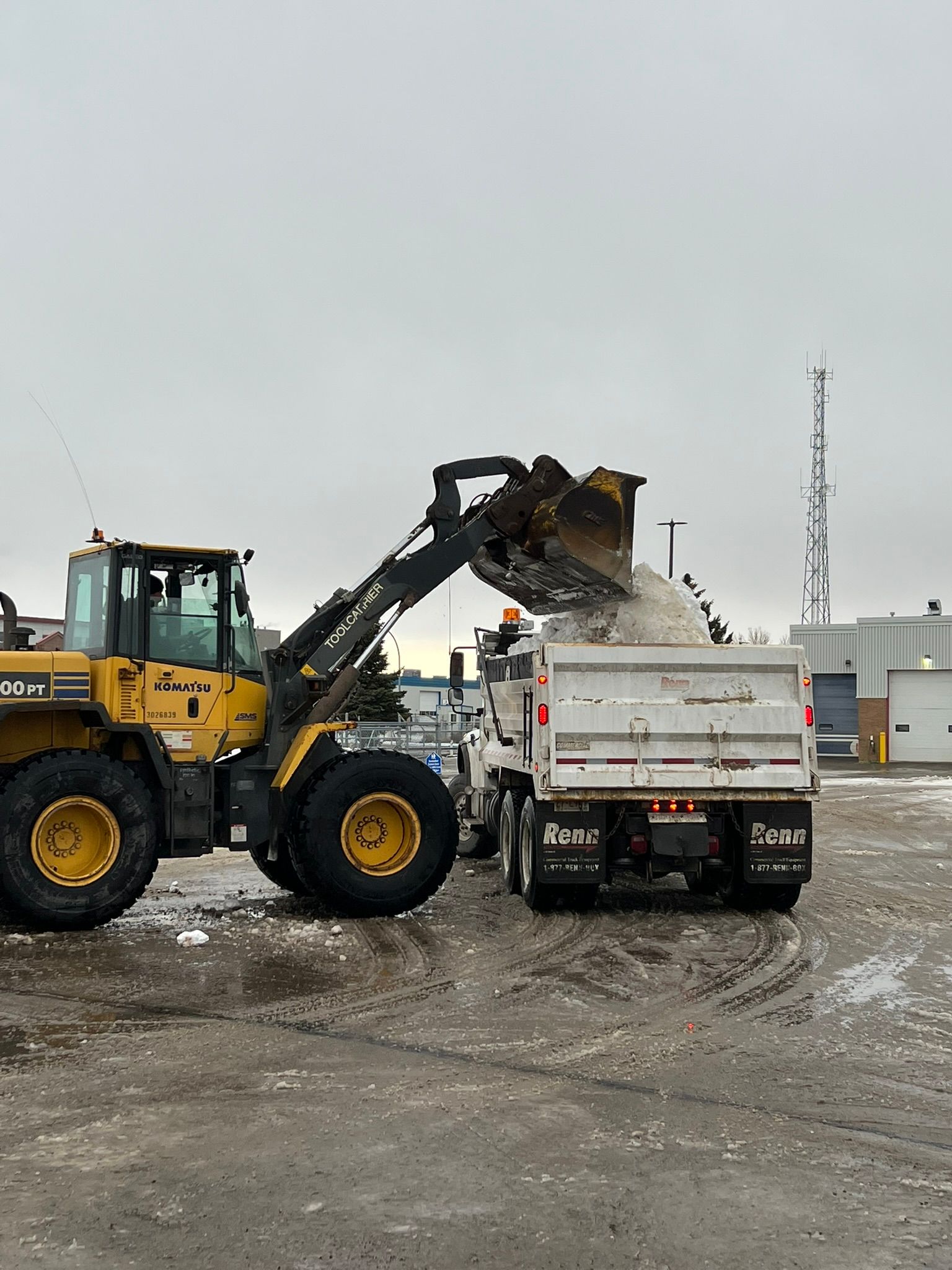 A bulldozer is loading snow into a dump truck.