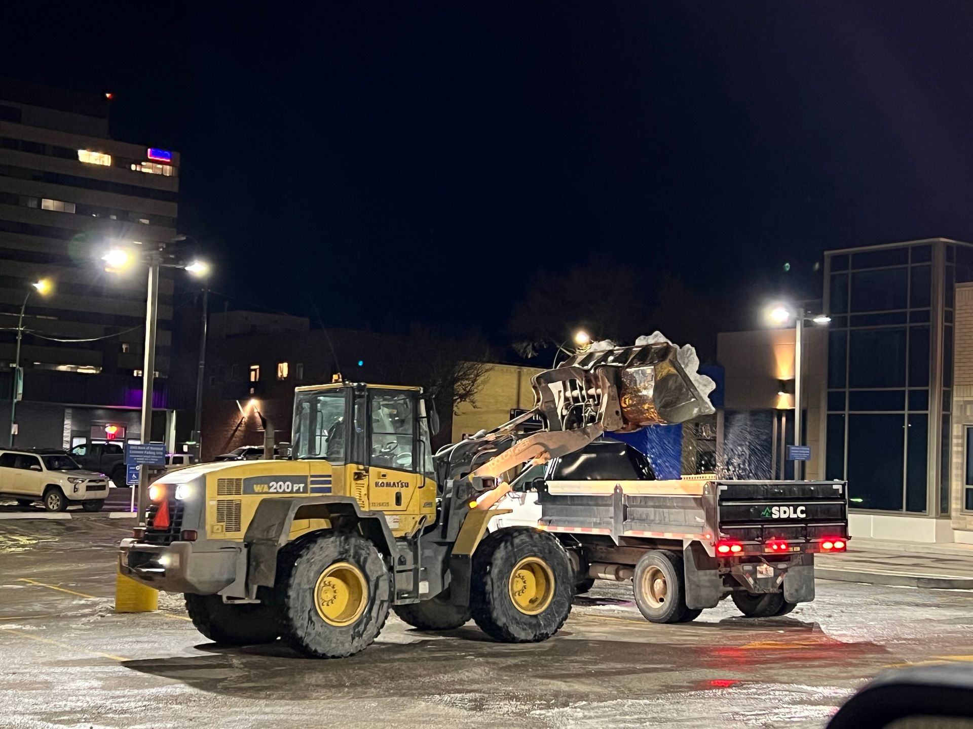 A truck is being towed by a bulldozer in a parking lot at night.