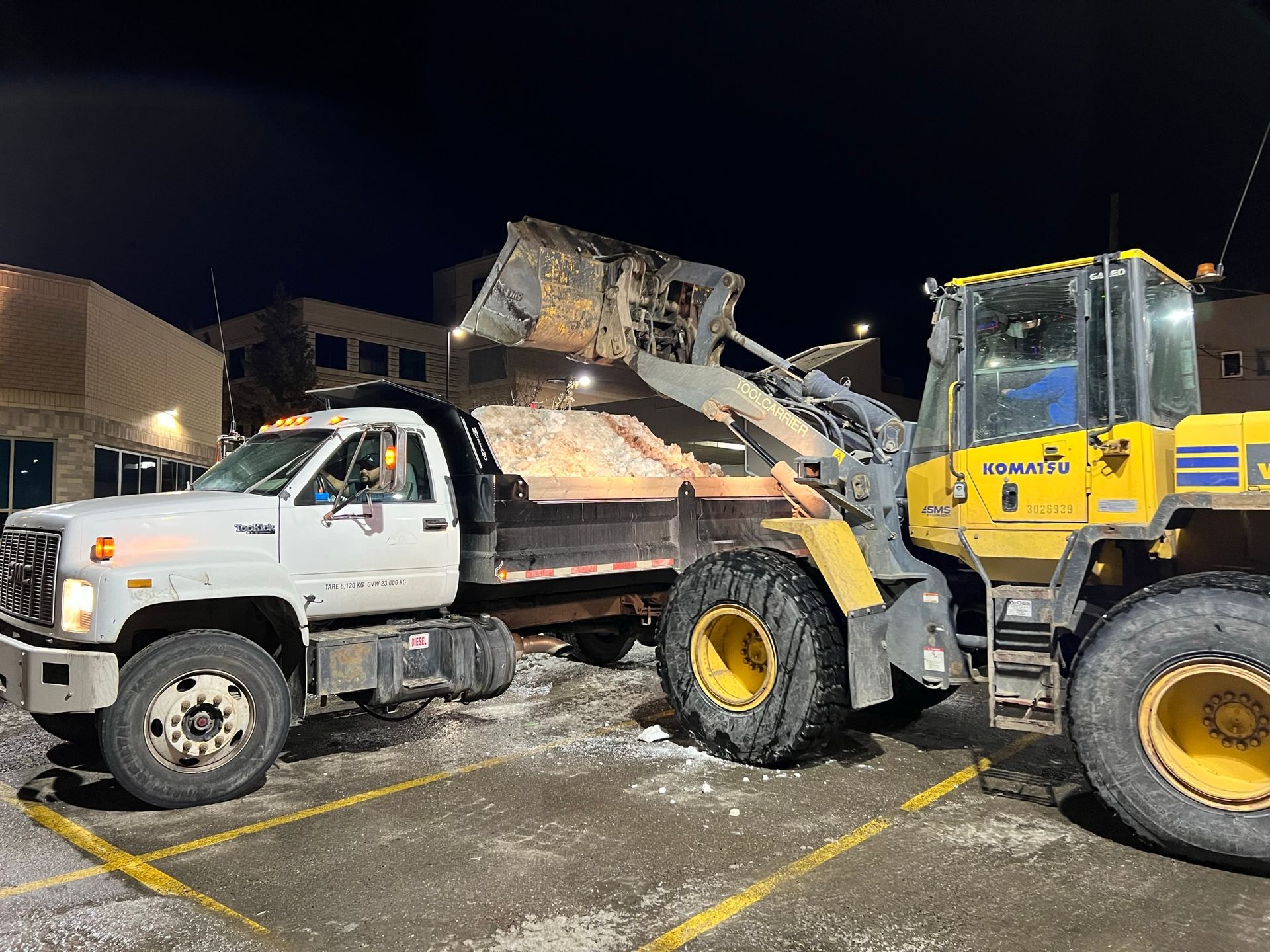 A dump truck and a wheel loader are parked in a parking lot at night.