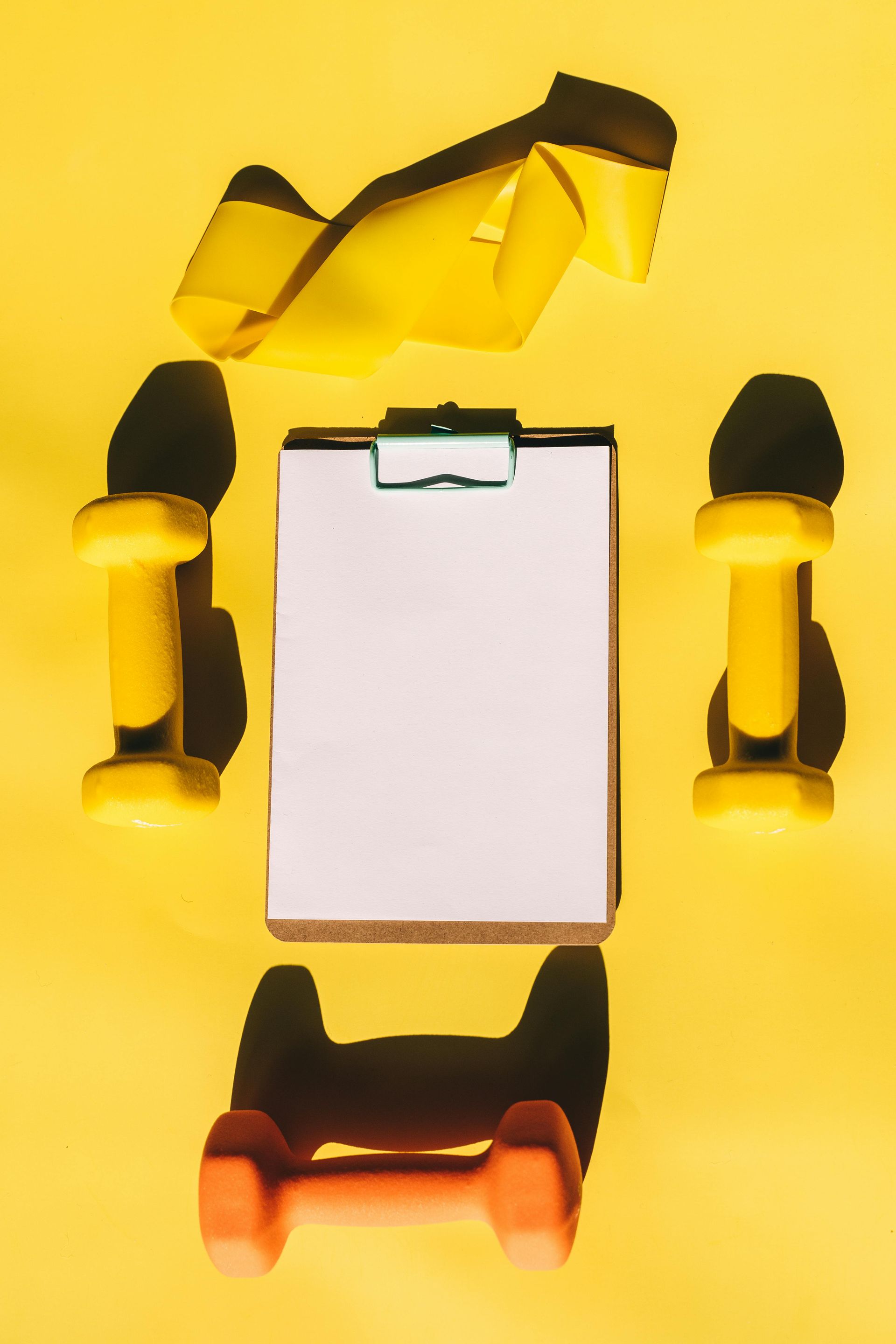 Bright yellow fitness-themed flat lay featuring two yellow dumbbells, a yellow resistance band.