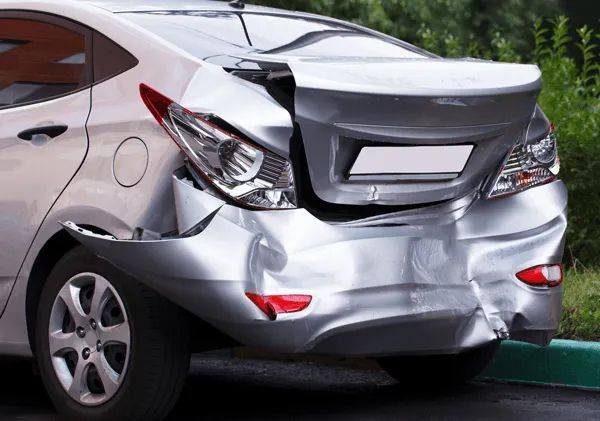 A silver sedan parked with significant rear-end damage, including a crumpled bumper and a partially detached trunk lid.