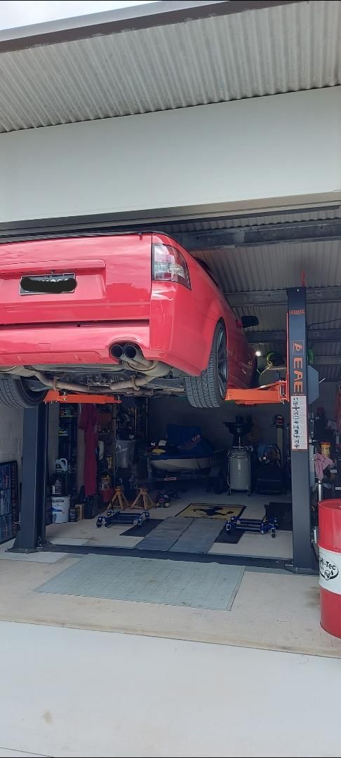 A Red Car Is Sitting on A Lift in A Garage — Coastal Mechanical Servicing and Repairs in Wurtulla, QLD