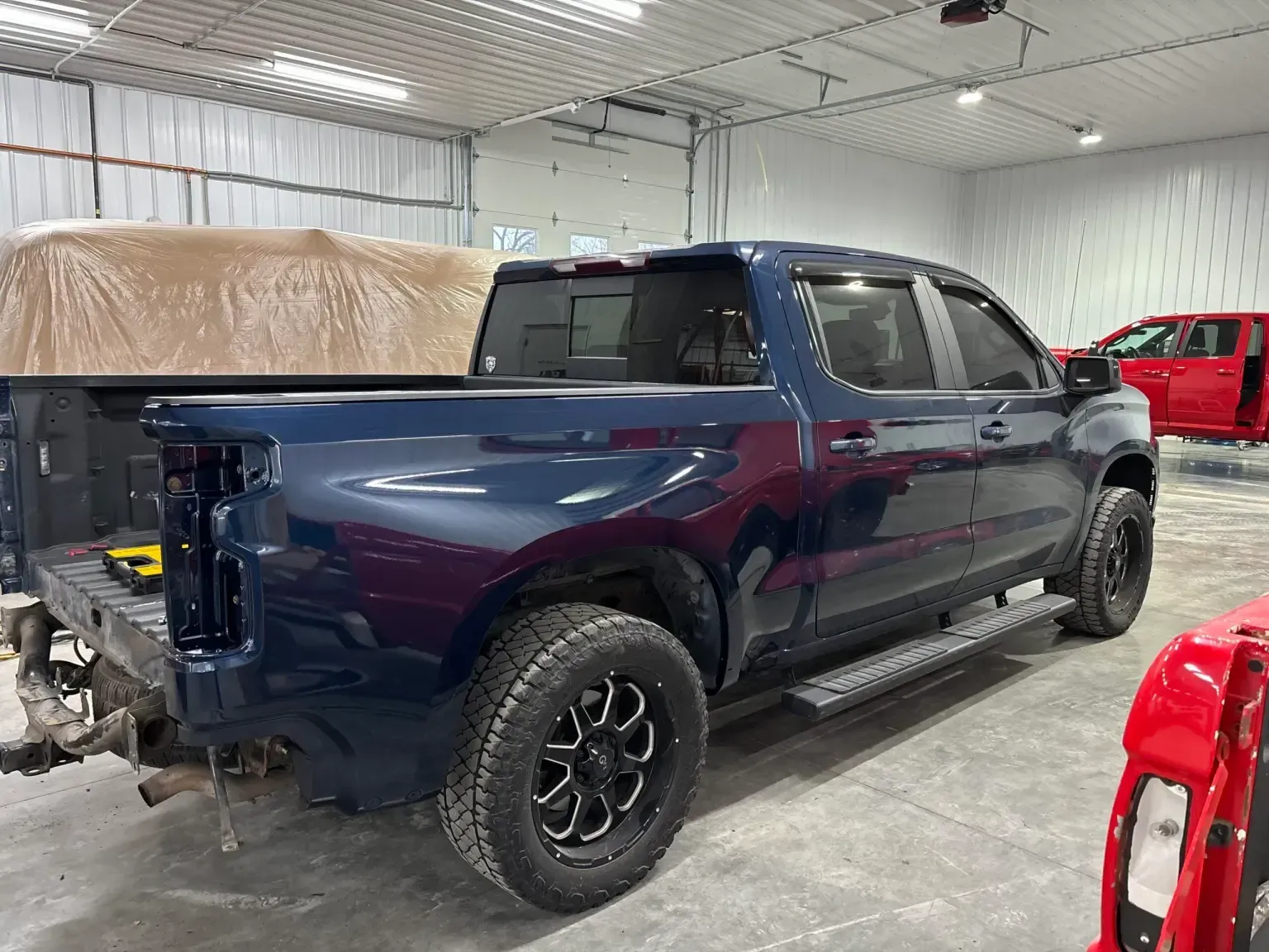 Dark blue pickup truck in a shop, rear bumper removed, black wheels, side steps.