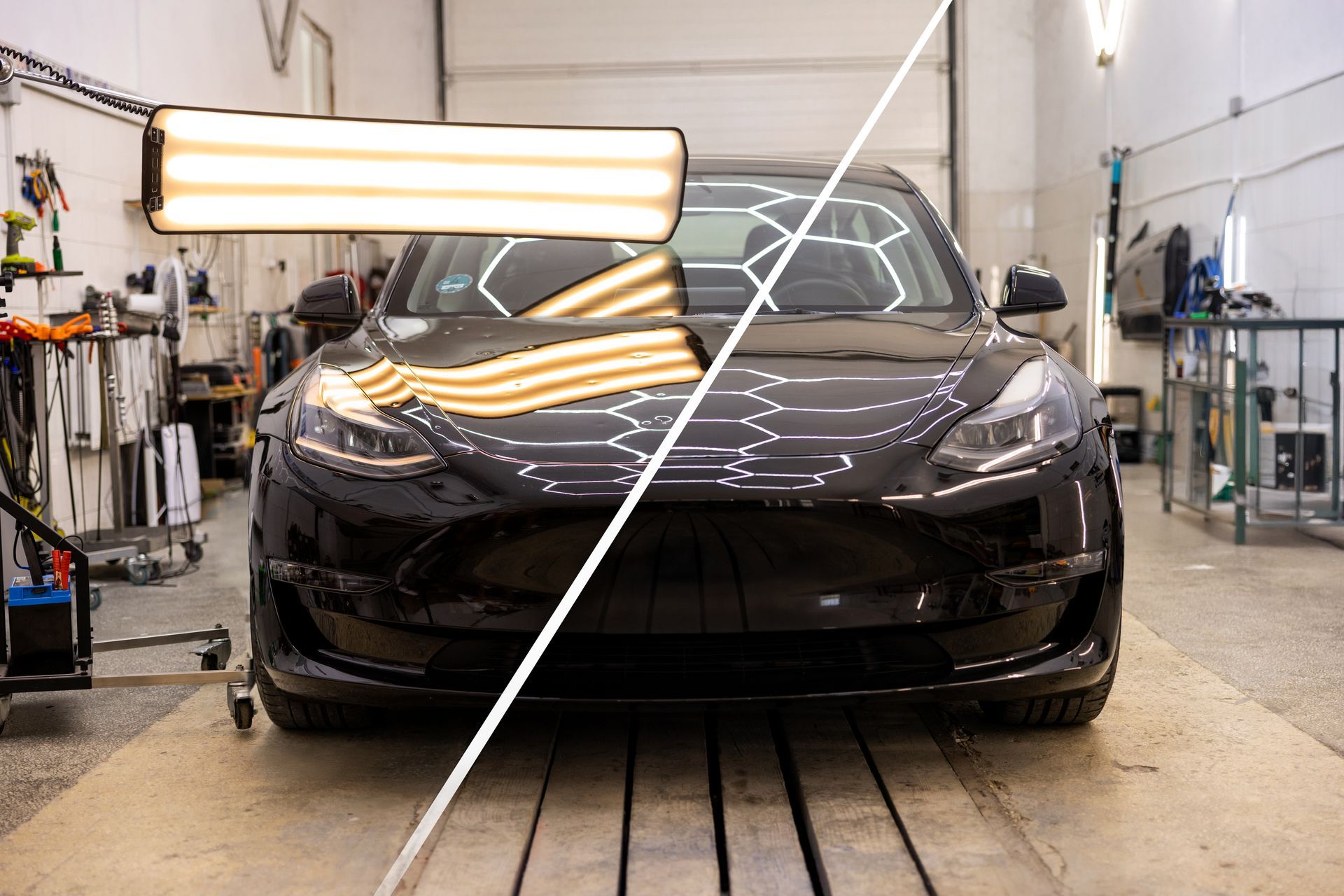 Black Tesla in repair shop, highlighted by dent repair light.