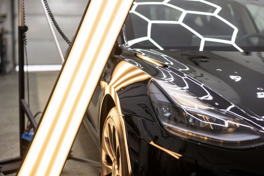 A person polishing a red car with a power tool, the car is taped in sections.