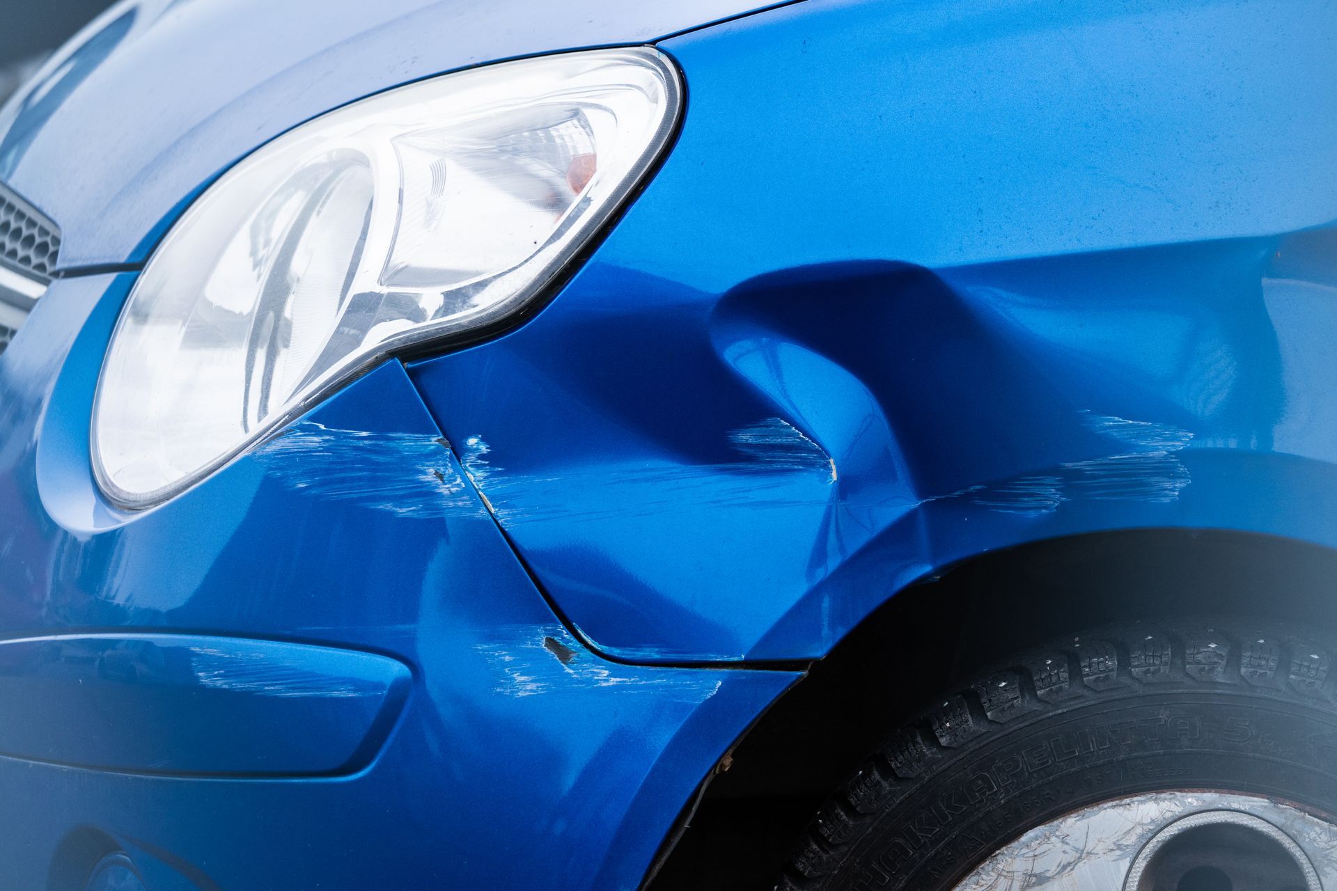 Close-up of a blue car’s front fender with visible dents and collision damage near the wheel.