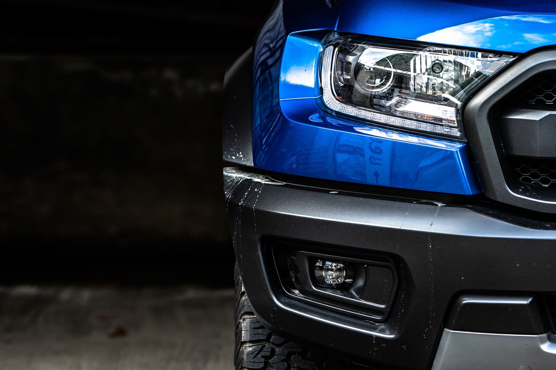 Blue Ford Raptor truck front end with a headlight and fog light.