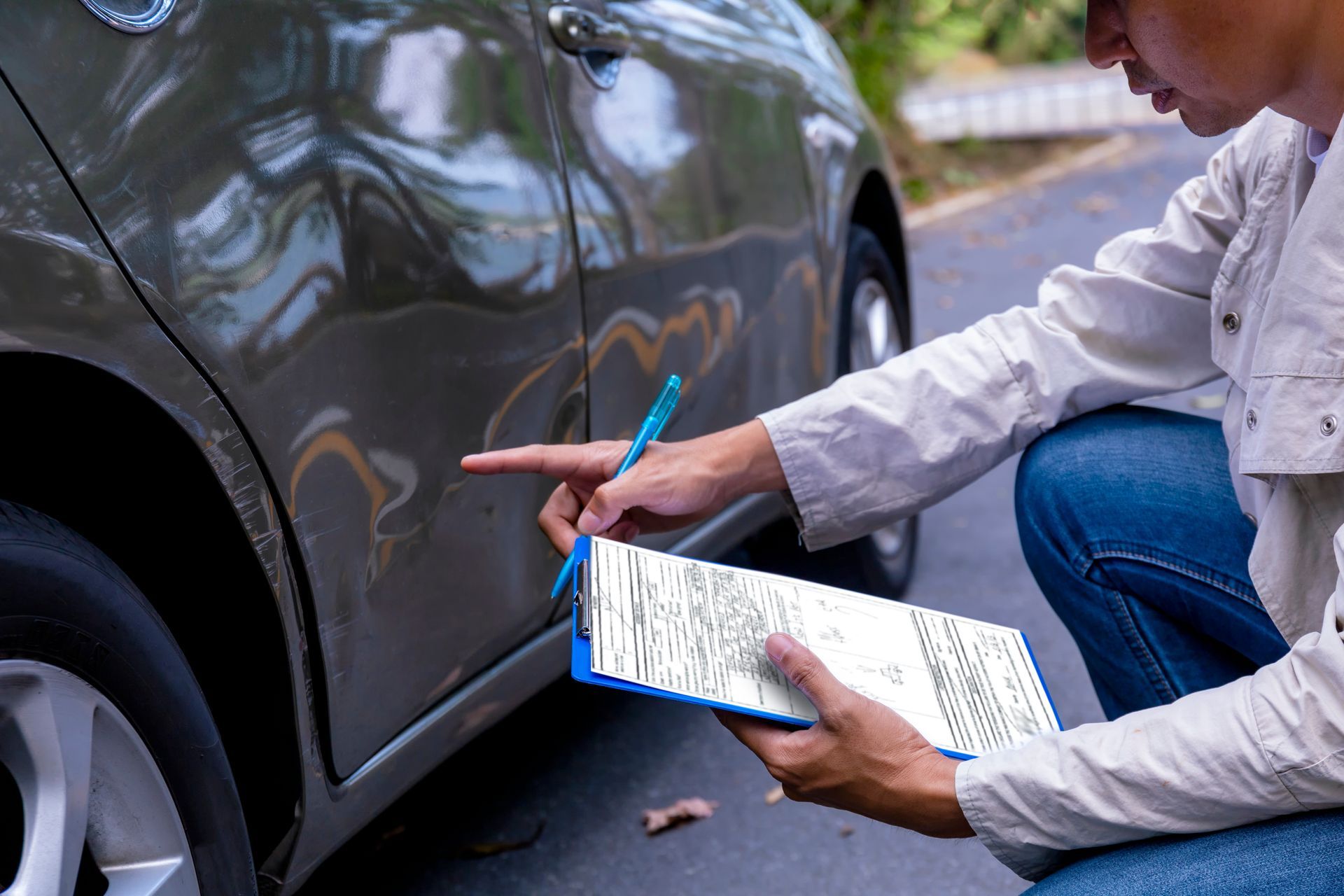 Person inspecting car damage, pointing at a dent on the side panel, writing on a clipboard.
