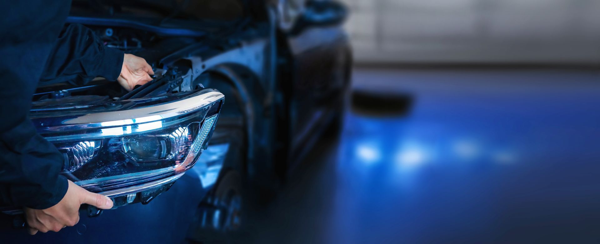 Auto body repair technician holding a vehicle headlight assembly during a collision repair.