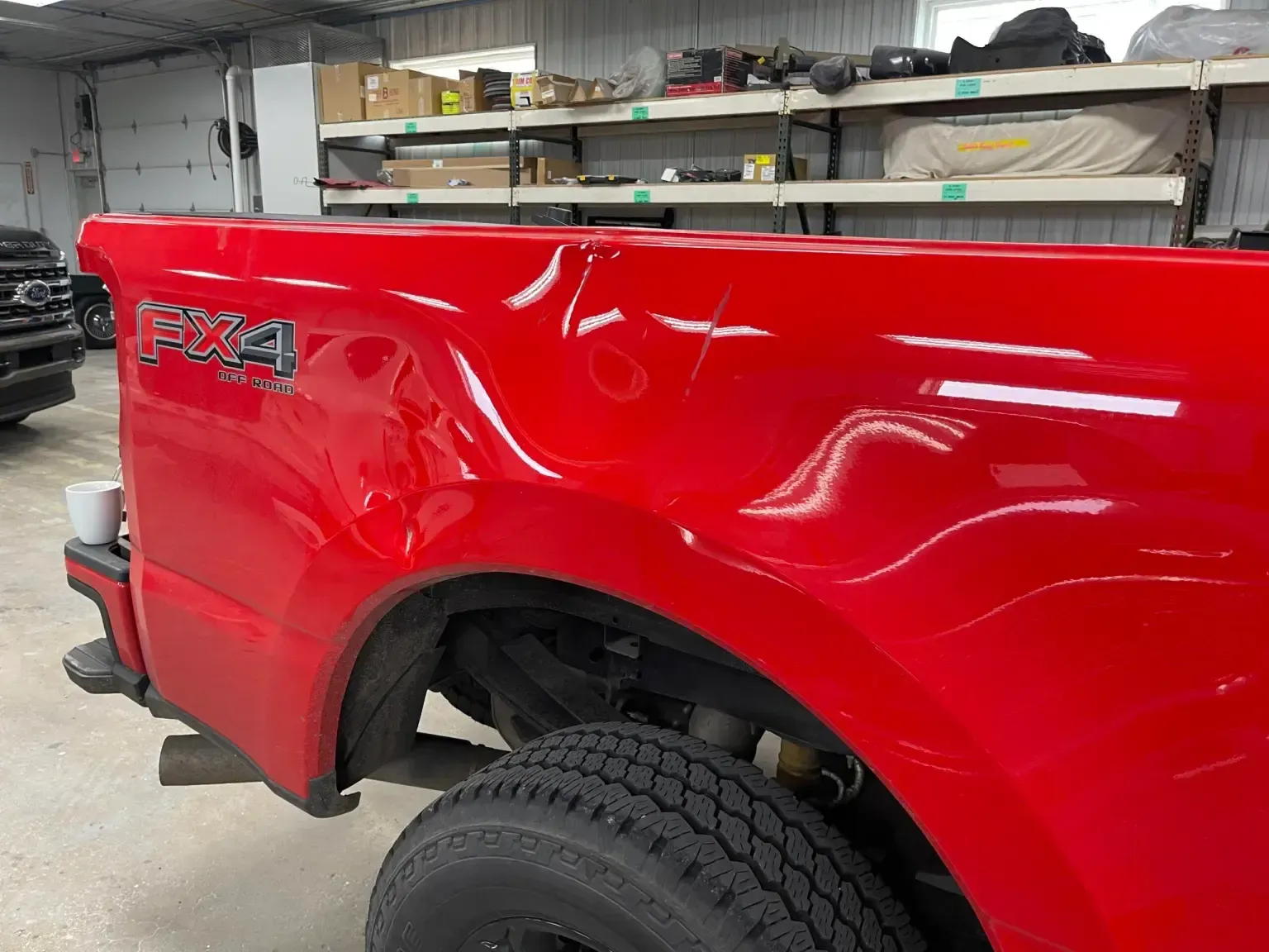 Red Ford truck bed with dents, a large tire visible.