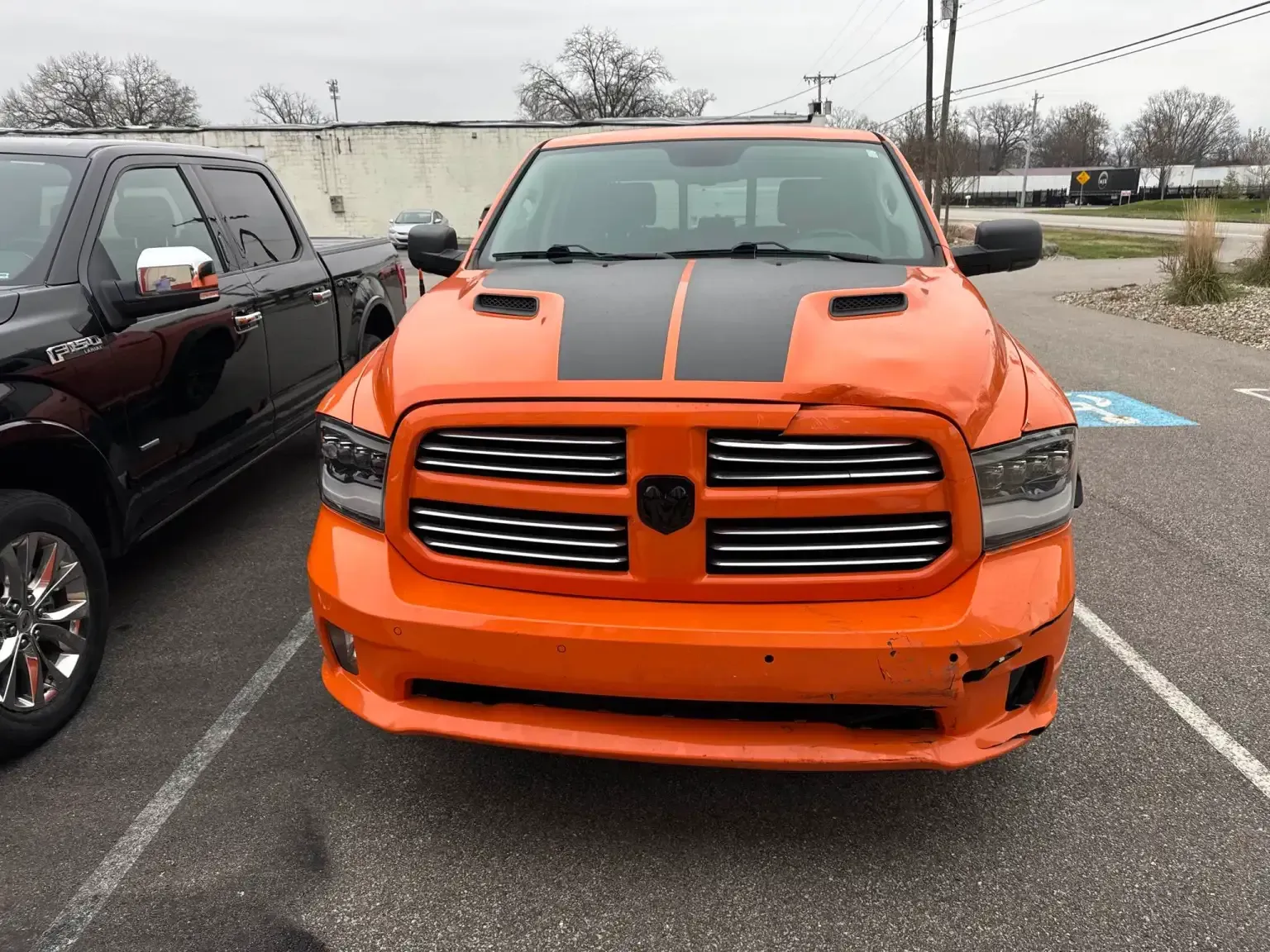 Bright orange Dodge Ram truck with black racing stripes parked in a lot.