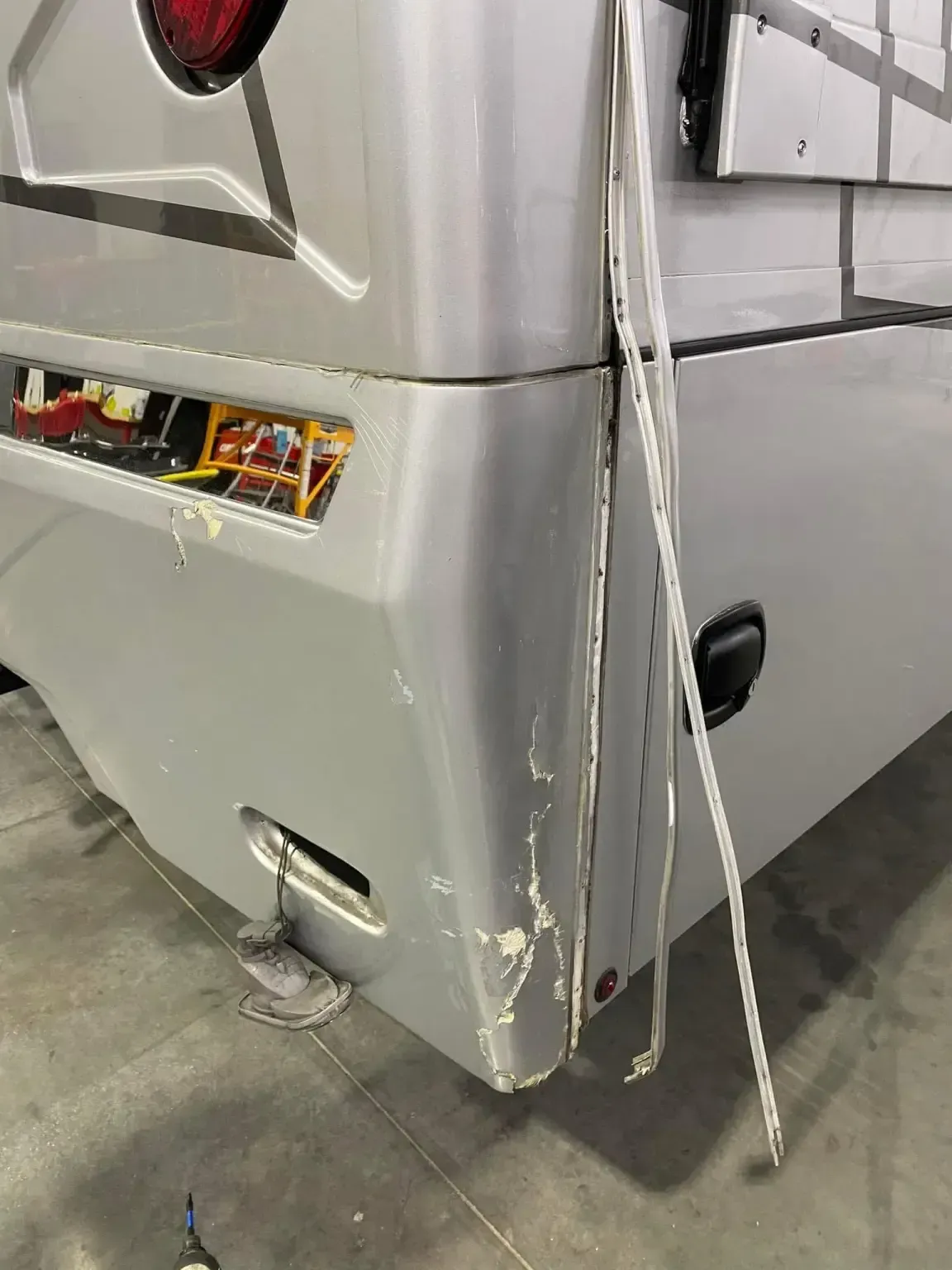 Damaged silver RV rear corner with dangling trim.