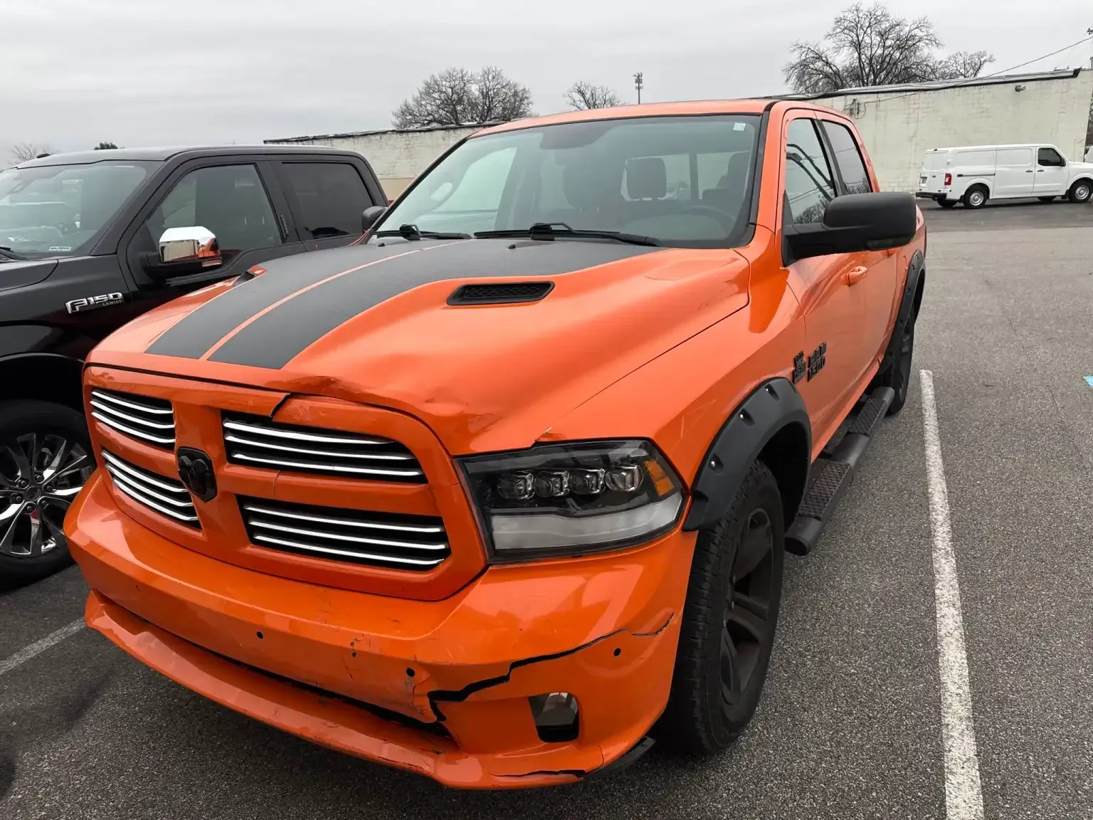 Orange Ram truck with black racing stripes and fender flares parked outside.