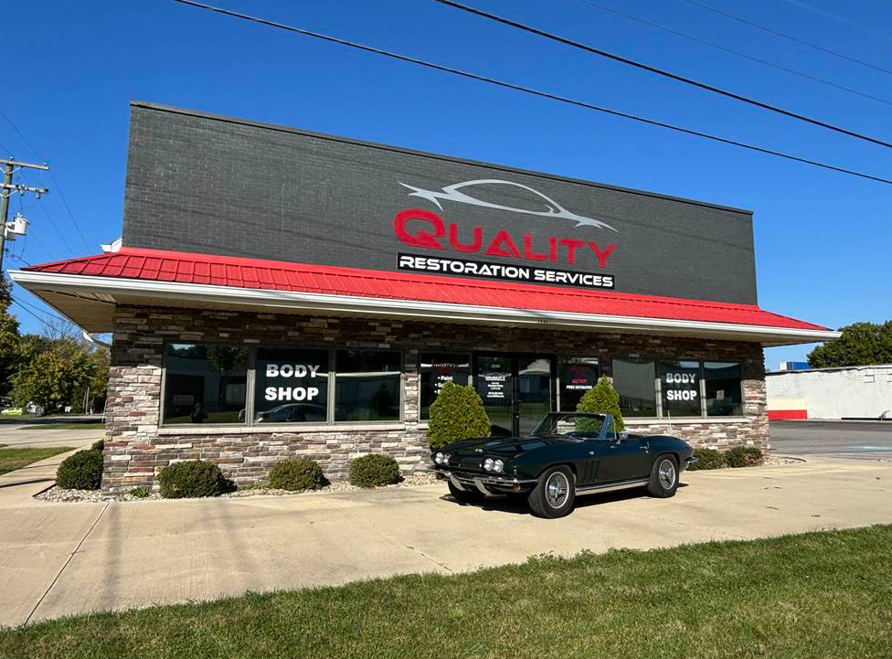 Person in protective suit sprays paint on a car door with a spray gun.