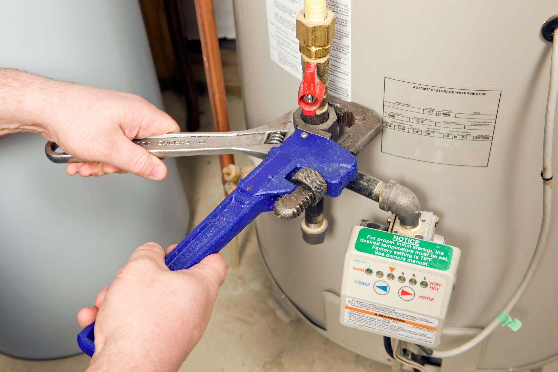 A person using a wrench on a water heater in a home setting.