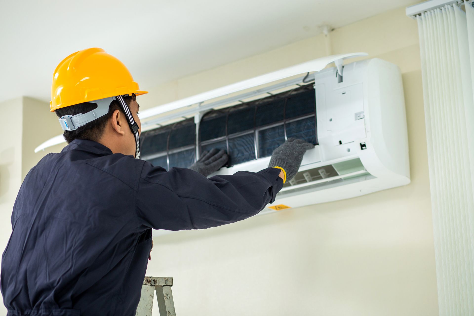 HVAC technician wearing safety gear cleaning an air conditioner filter on a wall.
