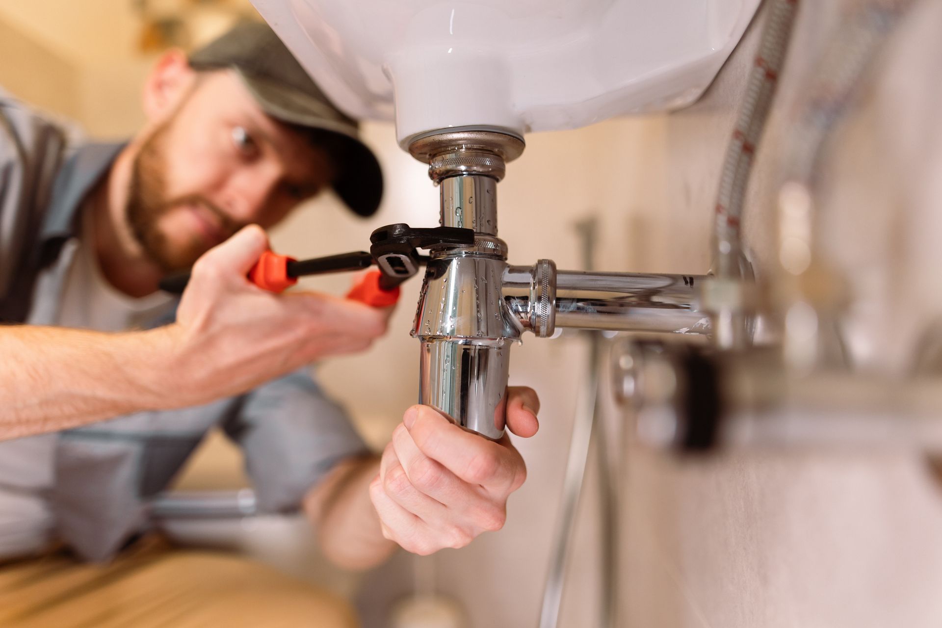 Plumber using a wrench under a sink, fixing pipes.